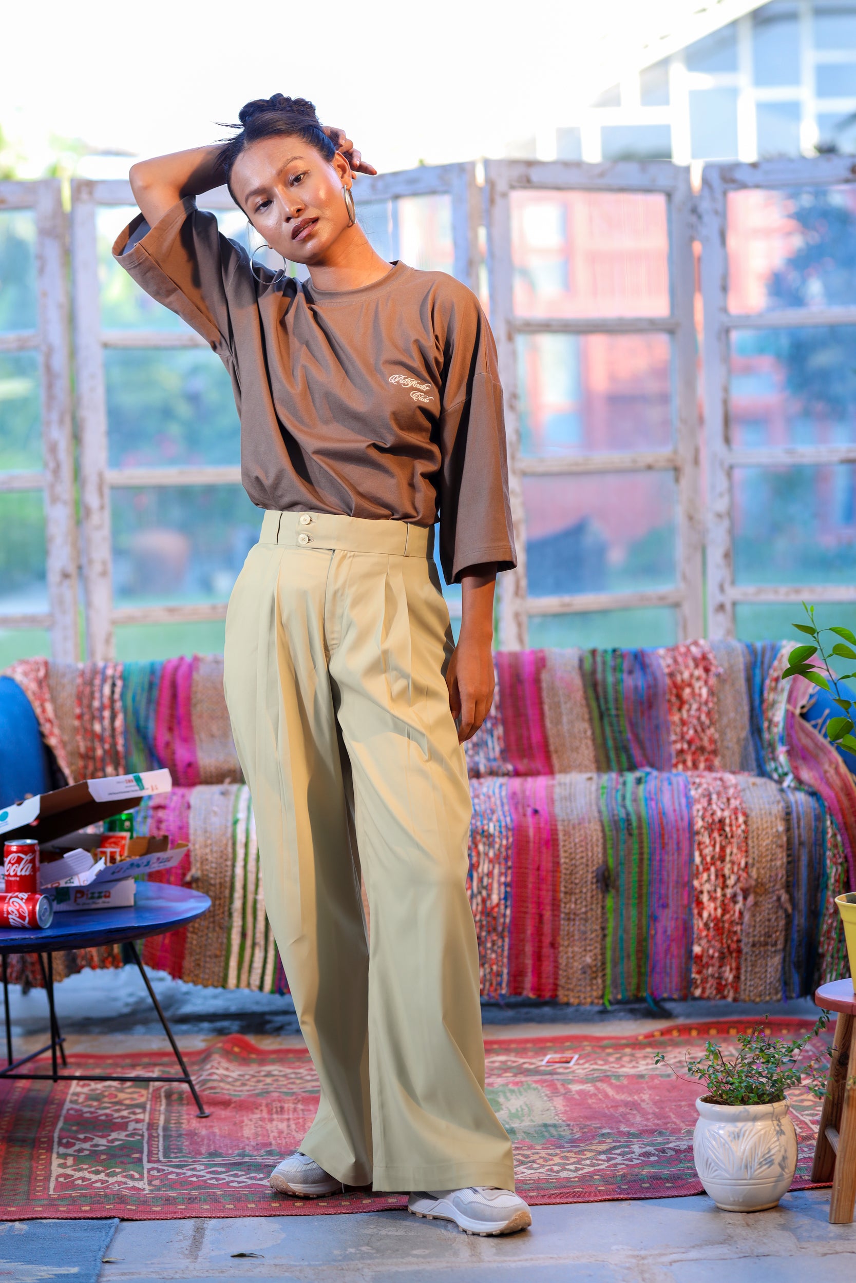 Woman in a brown top and beige pants standing in a room with colorful furniture and decor.
