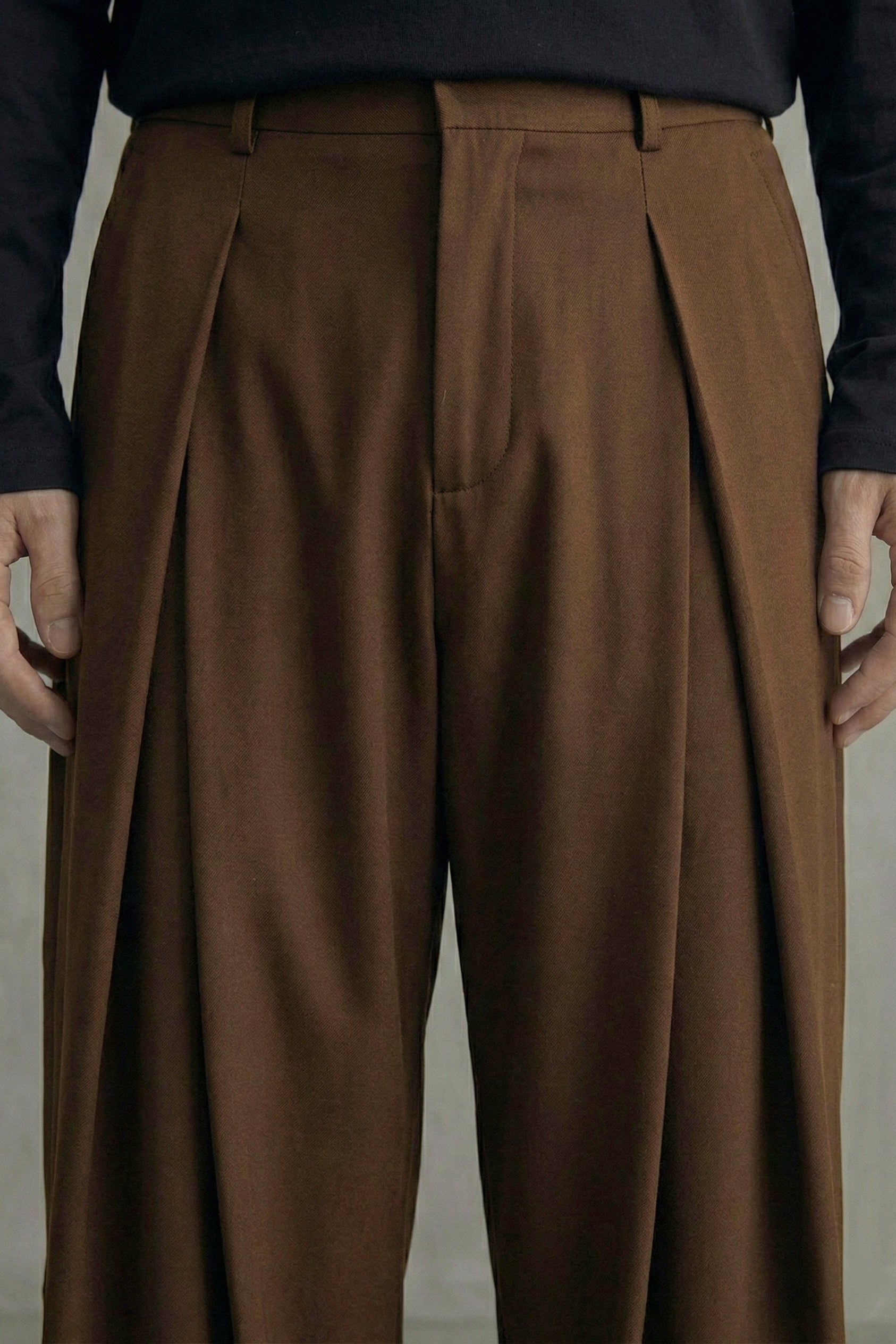 Brown pleated pants worn by a person against a neutral background