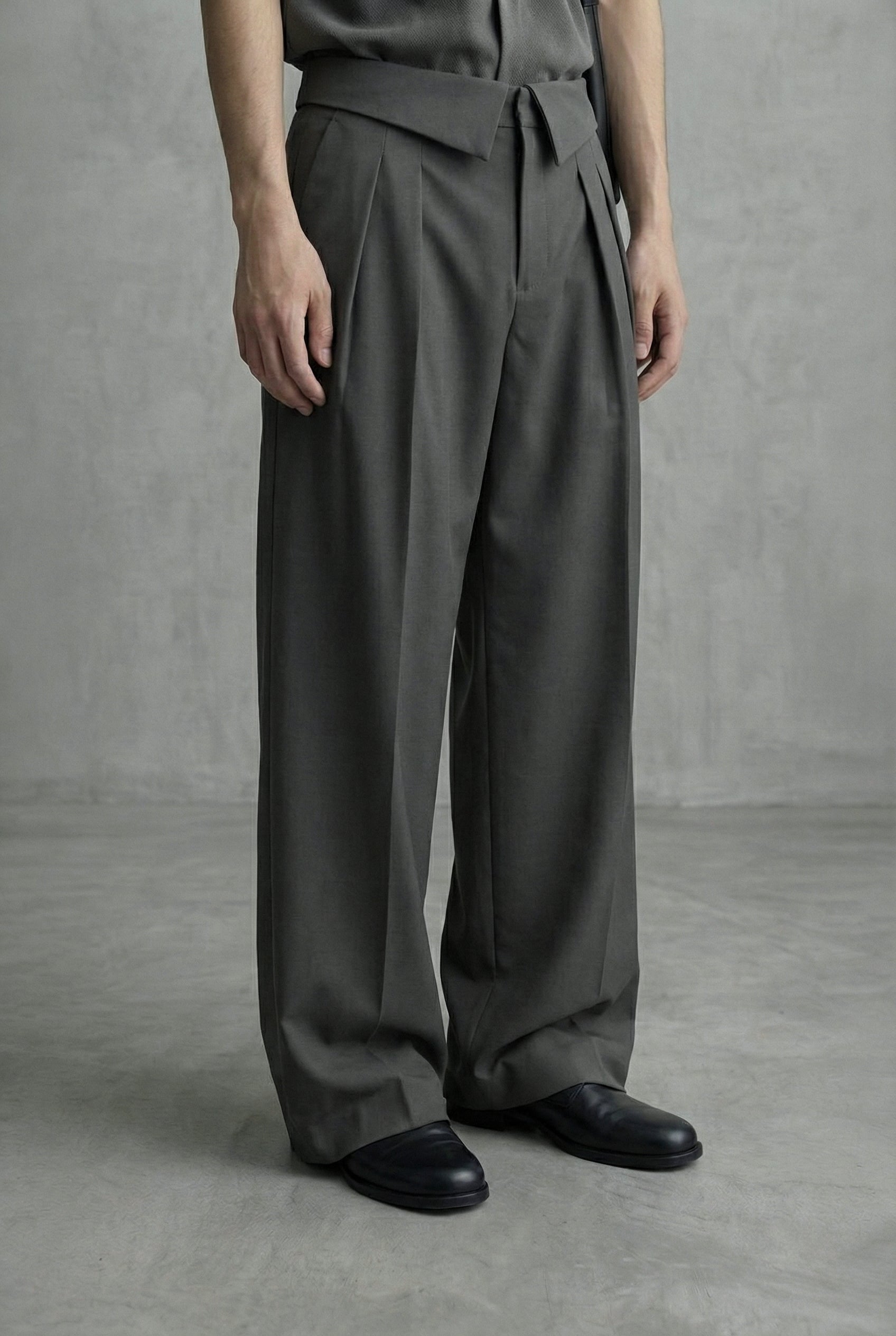 Person wearing dark gray wide-leg pants and black shoes on a plain background