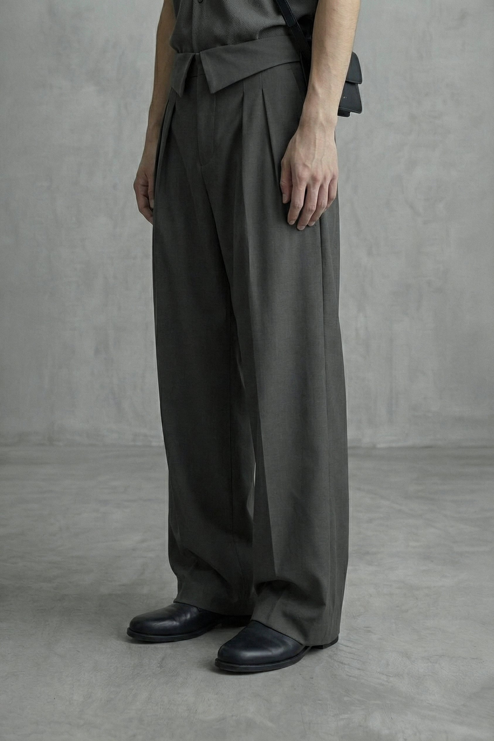 Person wearing a dark gray outfit with wide-leg pants against a plain background