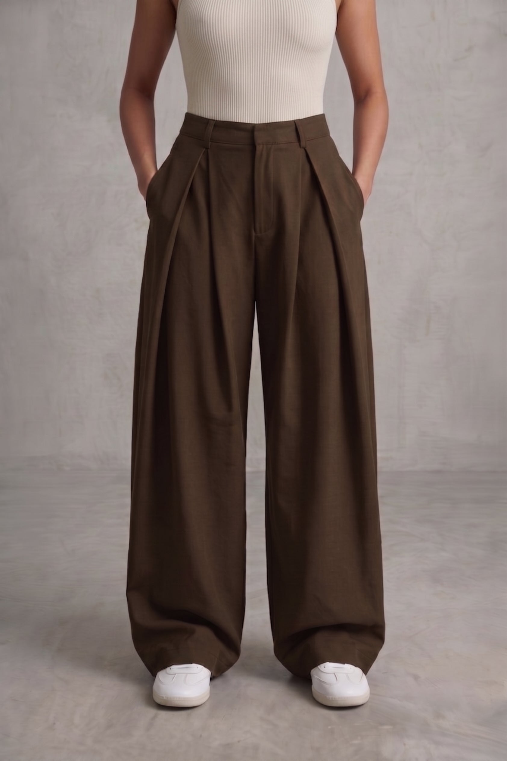 Person wearing brown wide-leg pants and a white top against a gray background