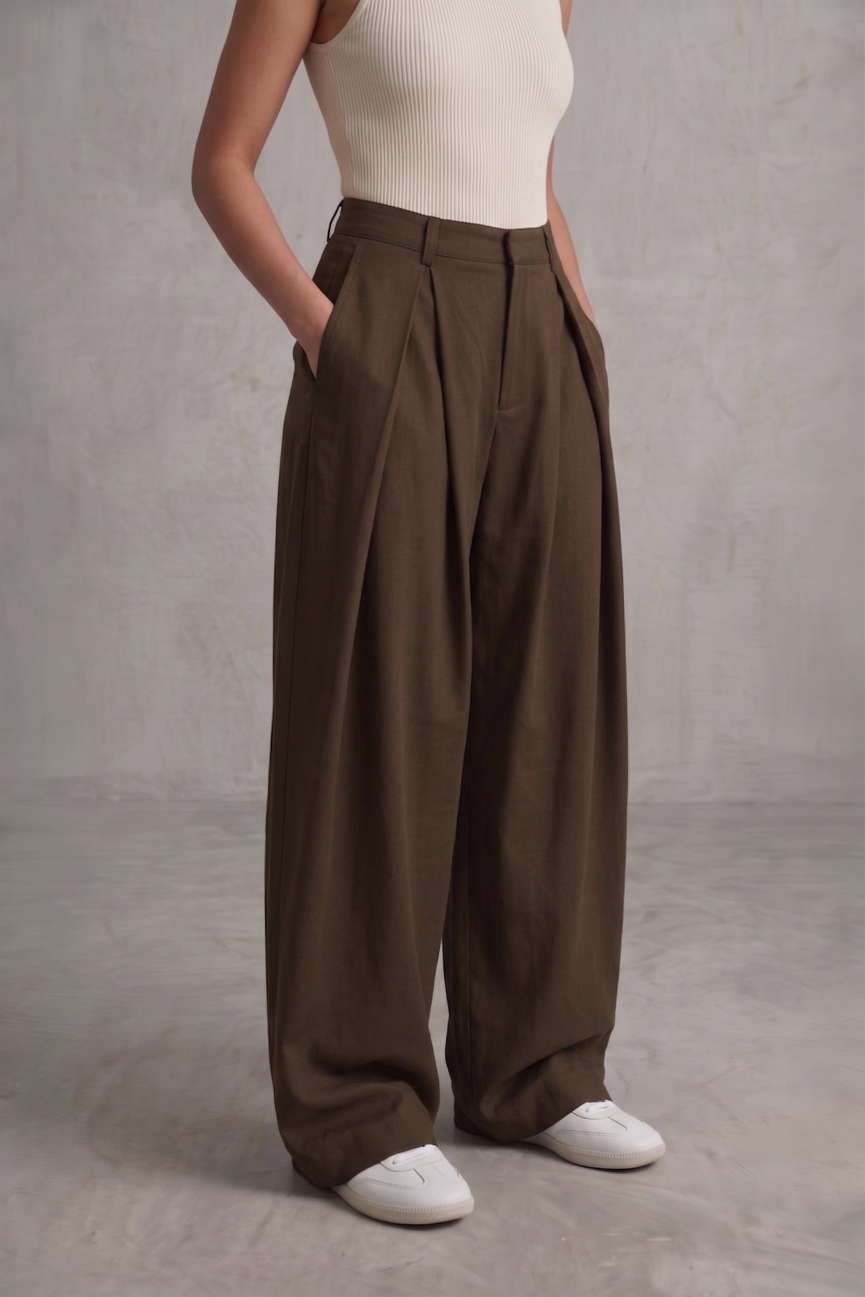 Person wearing brown wide-leg pants and a white top against a gray background