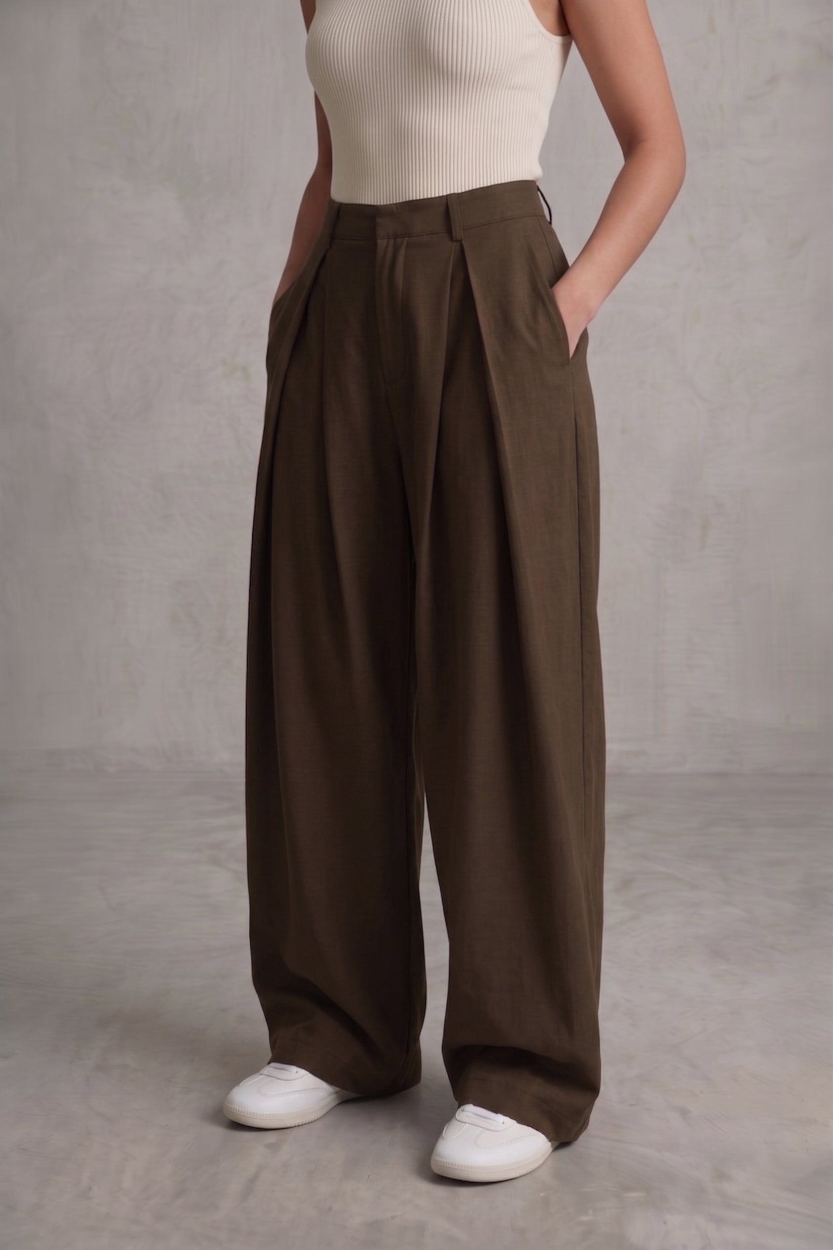 Person wearing brown wide-leg pants and a white top against a gray background