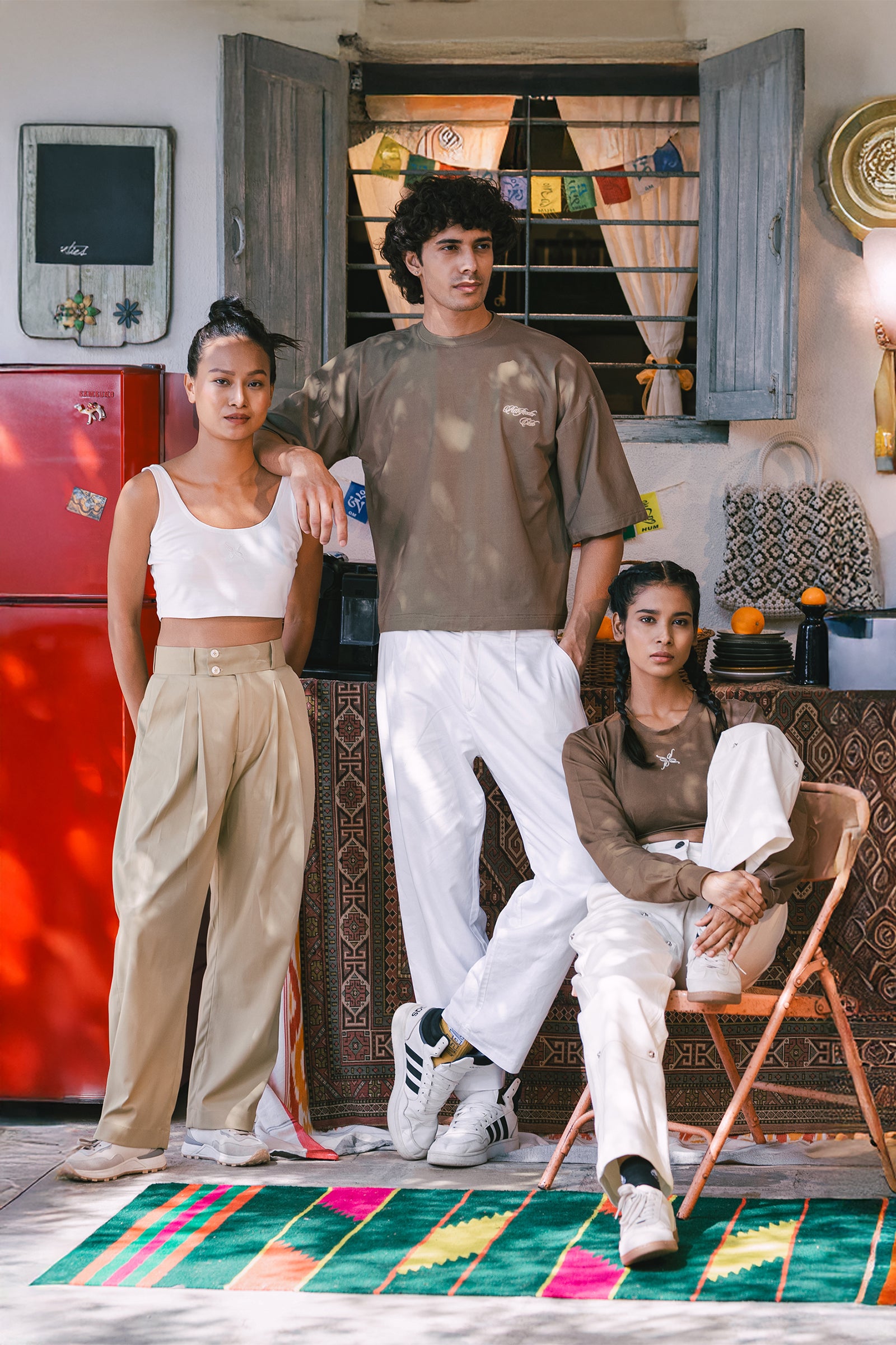 Three people posing in a room with colorful decor and a red refrigerator.