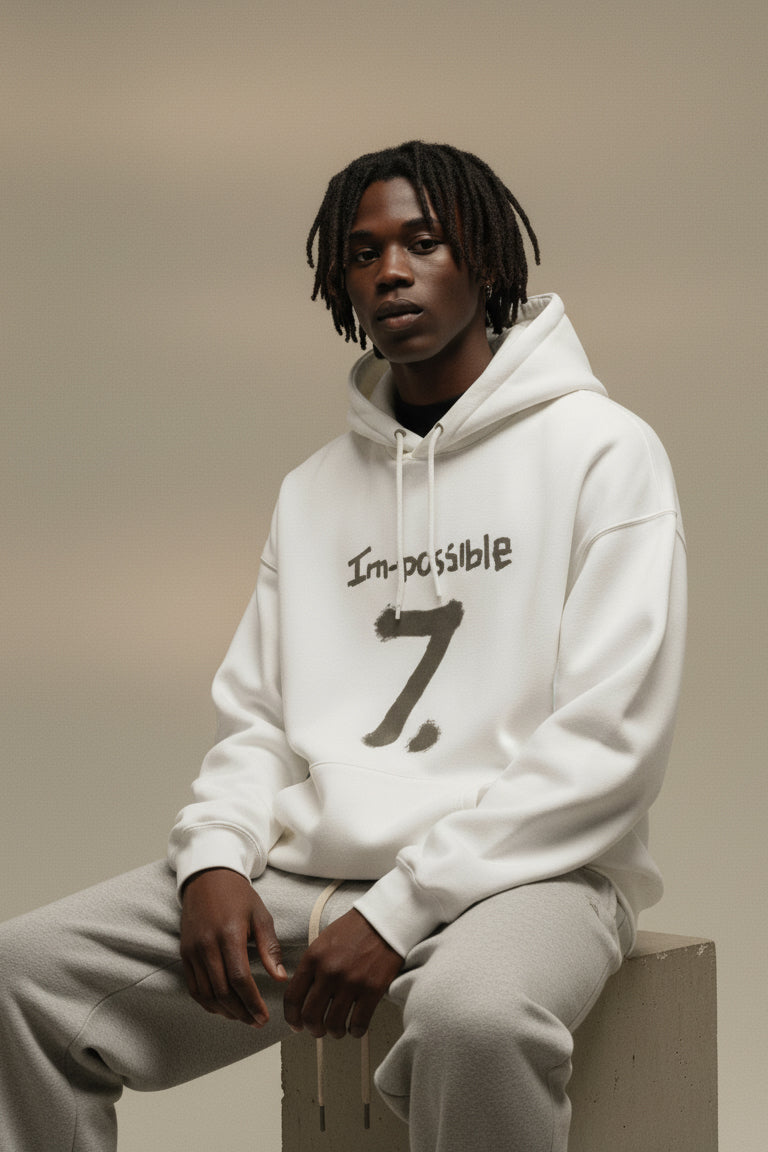 Person wearing a white hoodie with text sitting on a box against a beige background