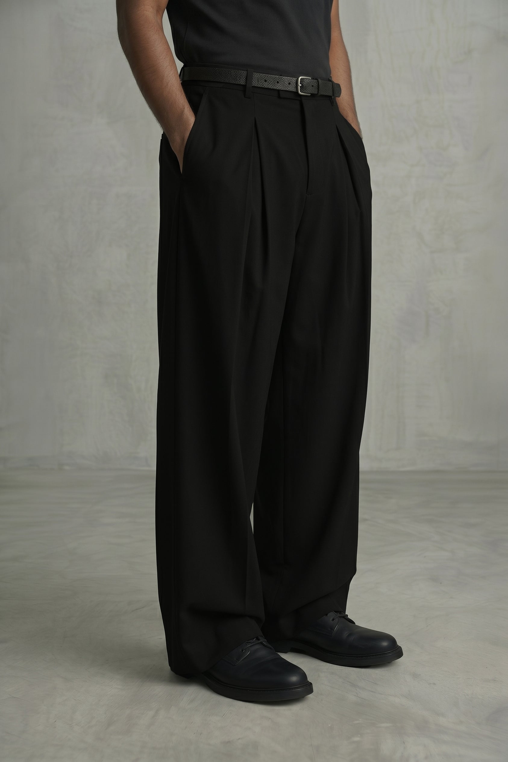 Person wearing black wide-leg pants and black shoes against a plain background
