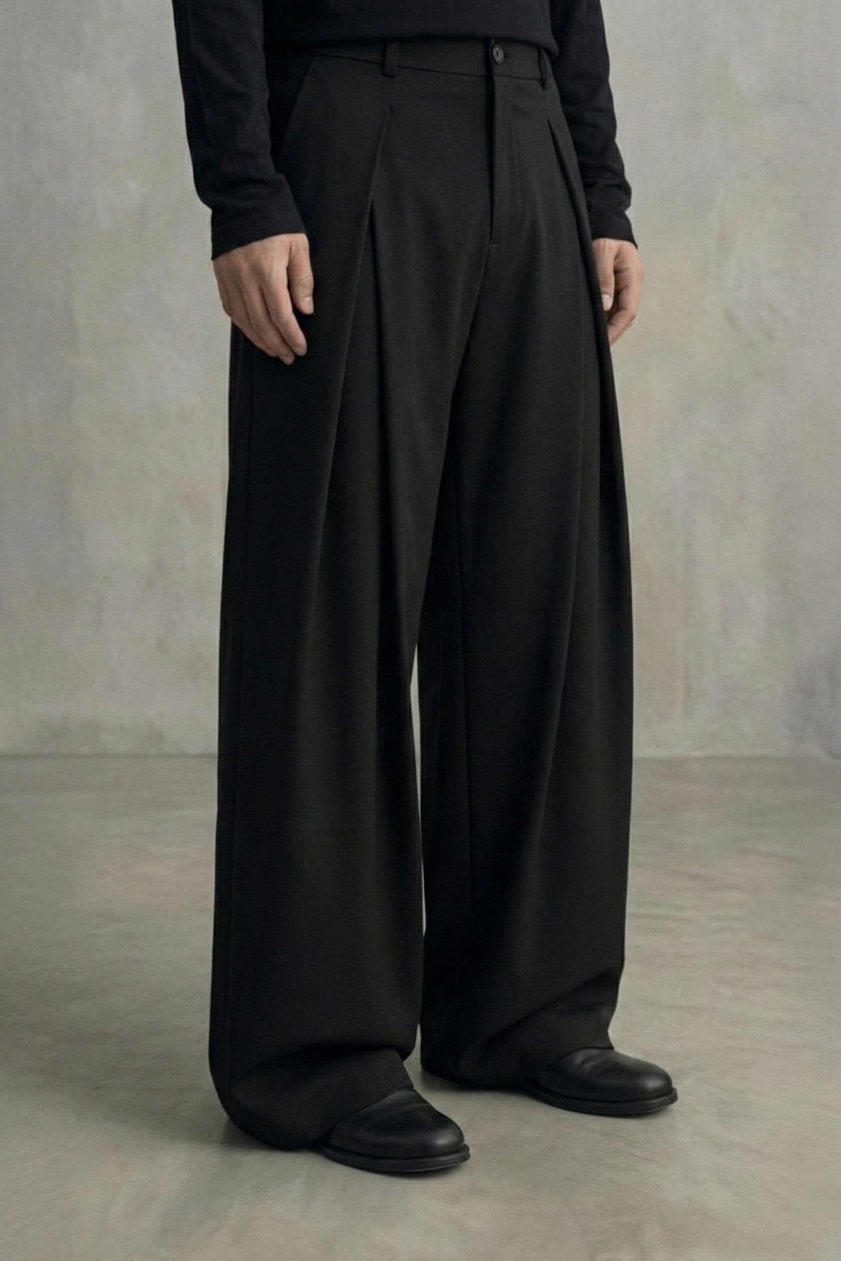 Person wearing black wide-leg pants and black shoes against a plain background