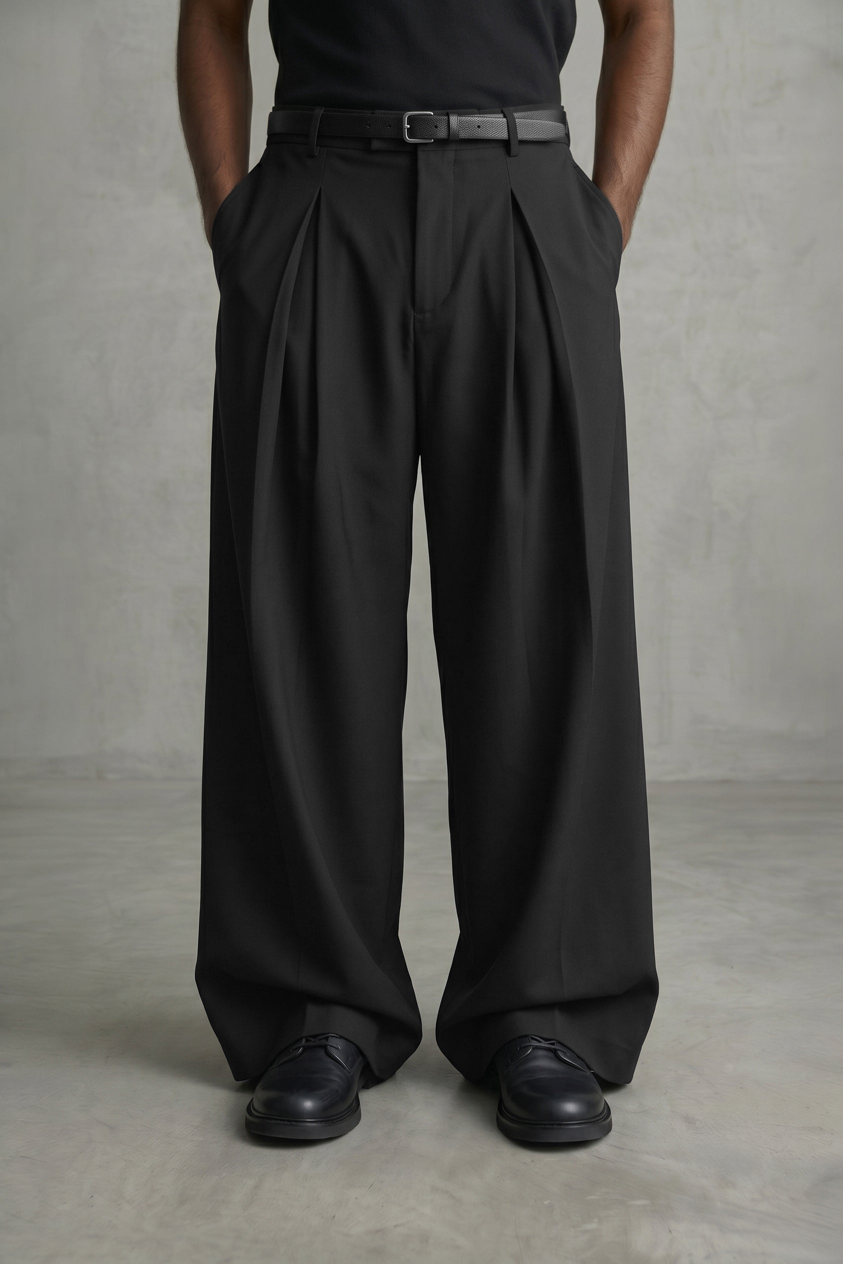 Person wearing black pleated pants and shoes on a gray background
