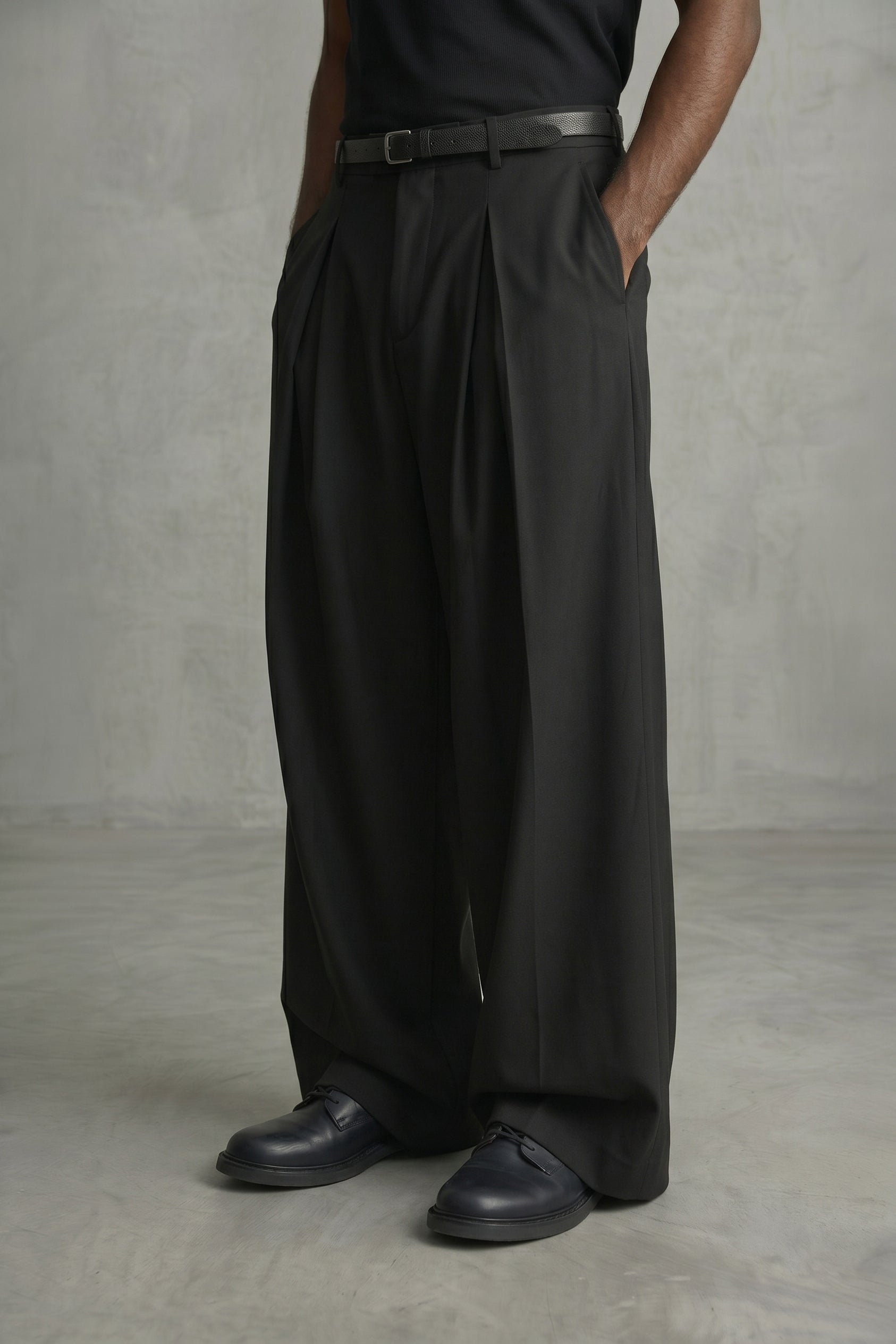 Person wearing black wide-leg pants and black shoes against a gray background