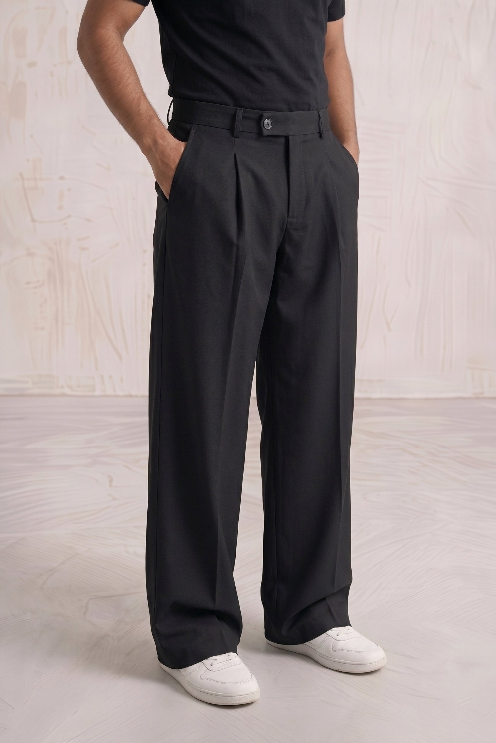 Person wearing black pleated pants and a black shirt on a light wooden floor.