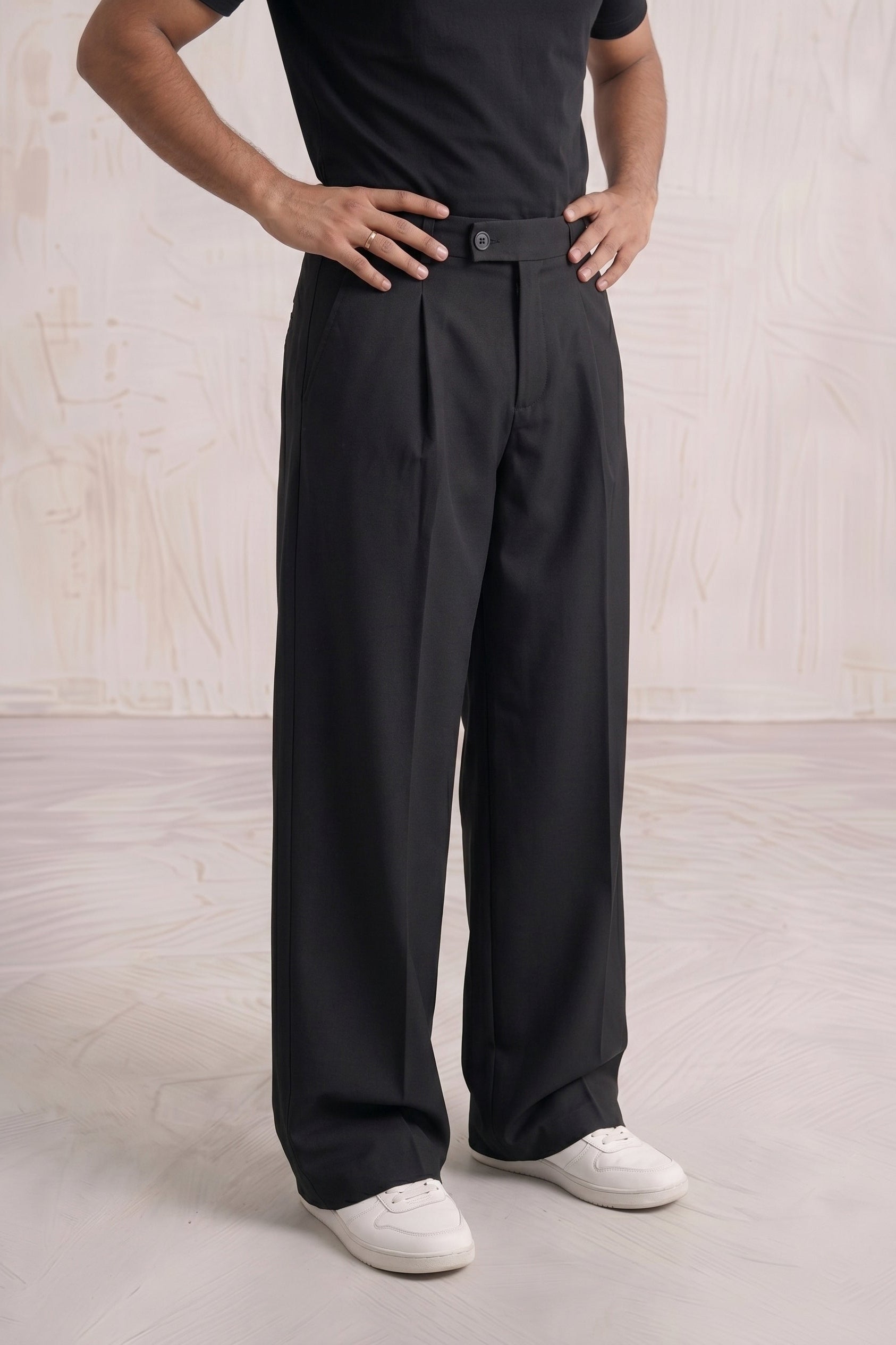 Person wearing black pleated pants and a black shirt on a light wooden floor.