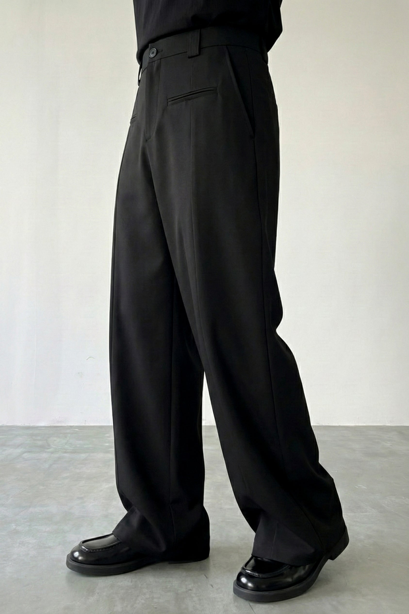 Person wearing black wide-leg pants and shoes on a plain background