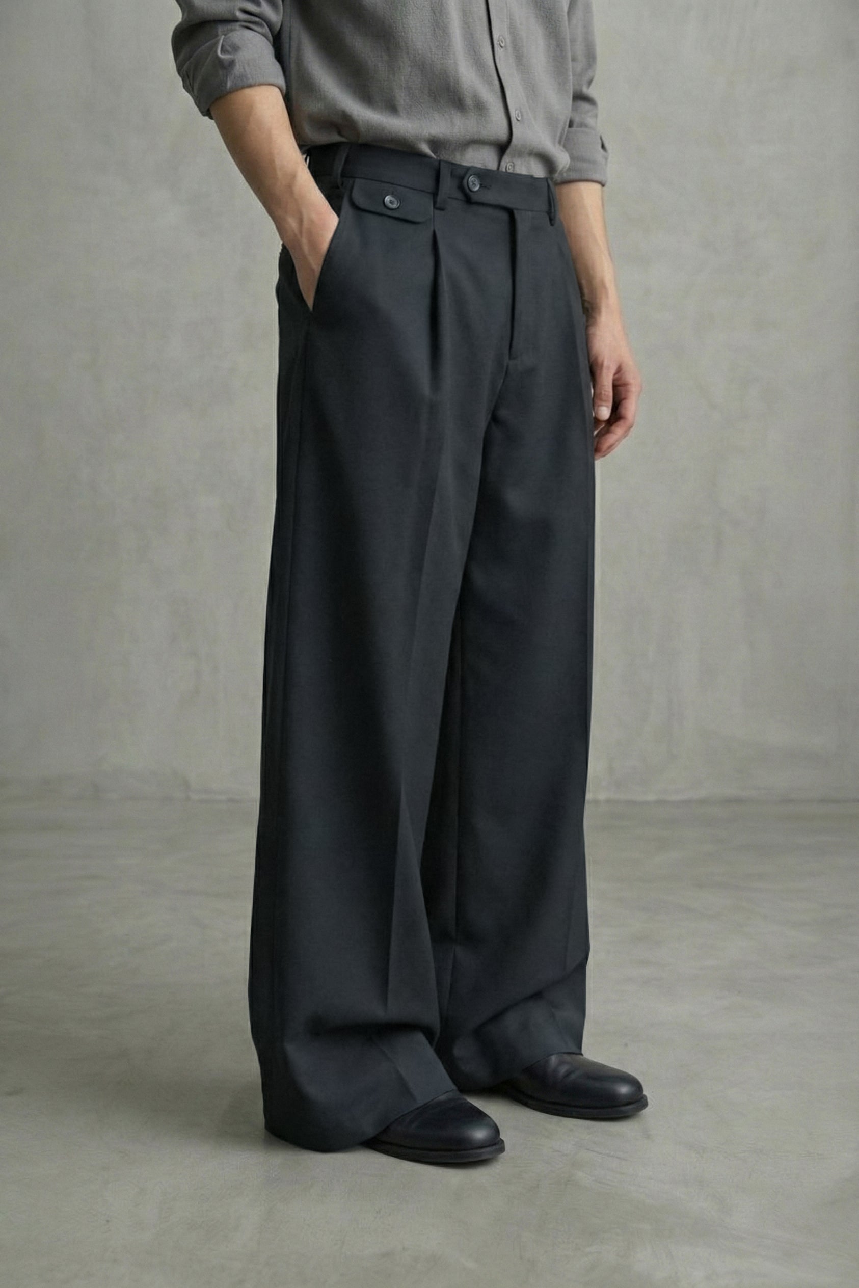 Person wearing dark gray pleated pants and a gray shirt against a plain background