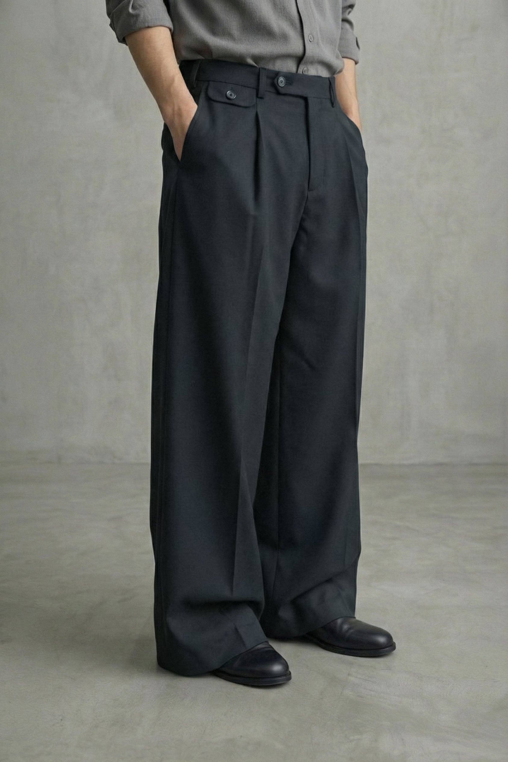 Person wearing dark pleated pants and a gray shirt against a plain background