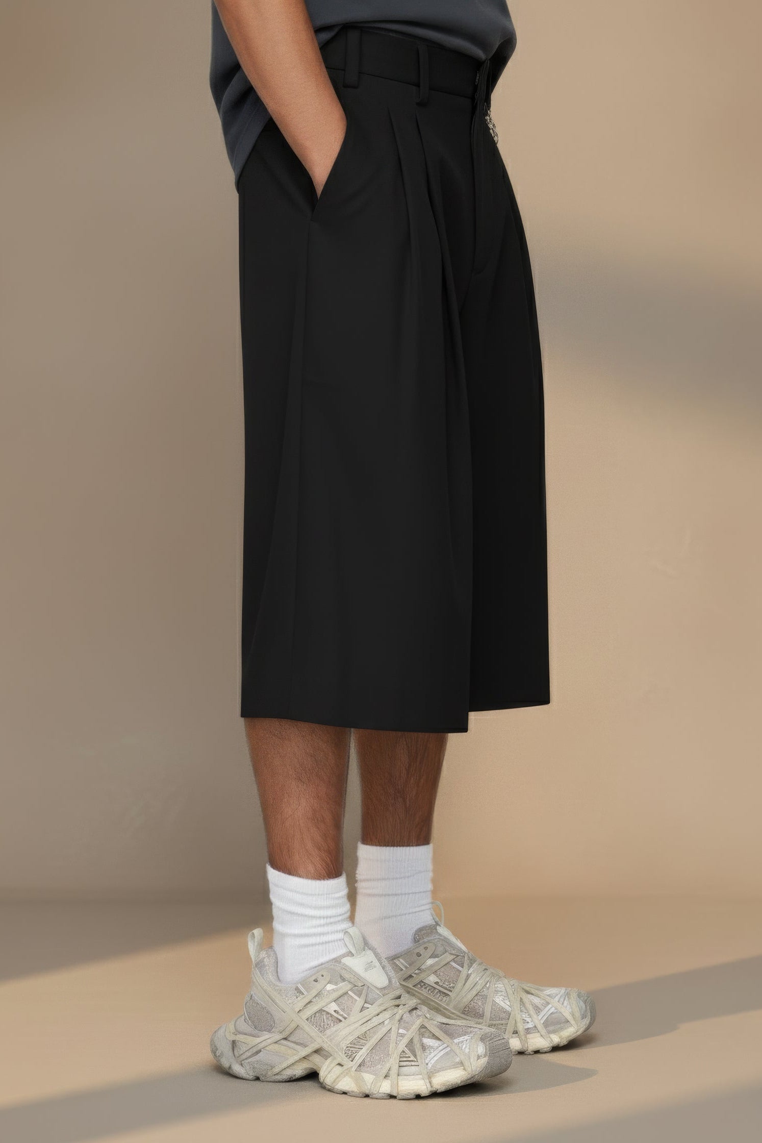 Person wearing black pleated shorts and white sneakers on a beige background