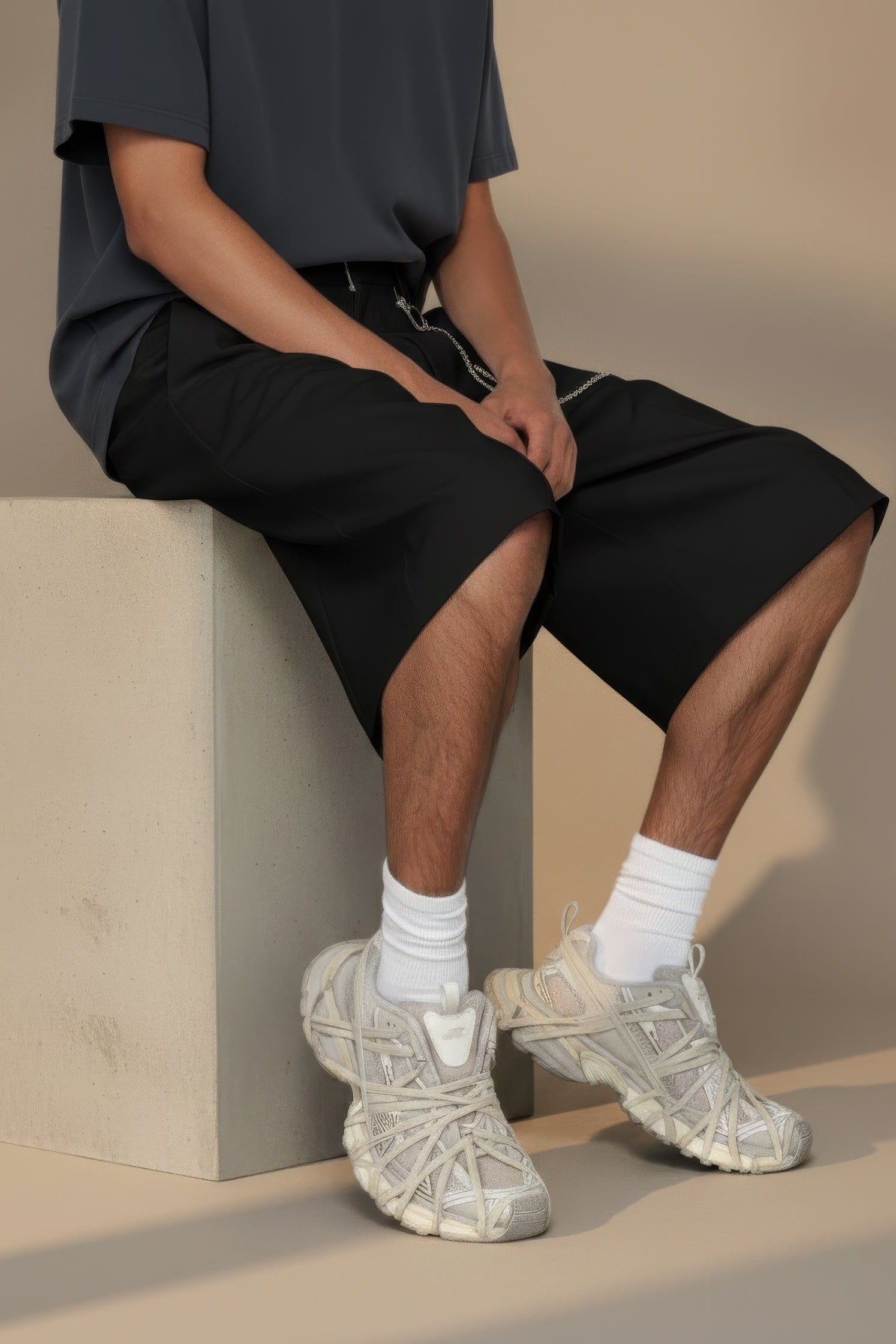 Person wearing black shorts and beige sneakers sitting on a block with a neutral background