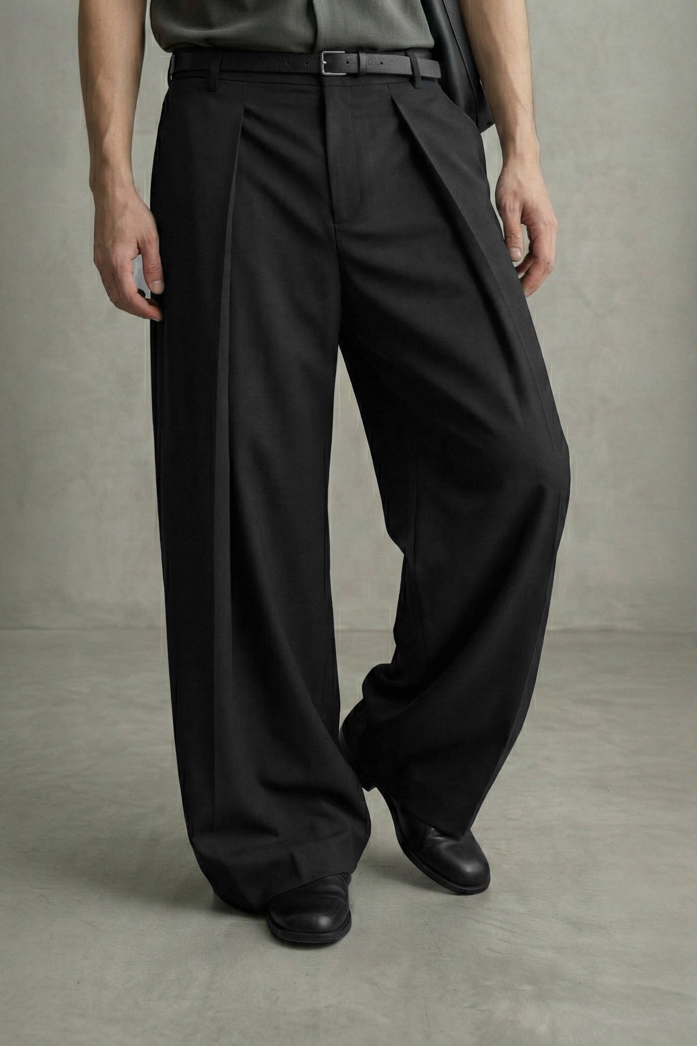 Person wearing black pleated pants on a neutral background