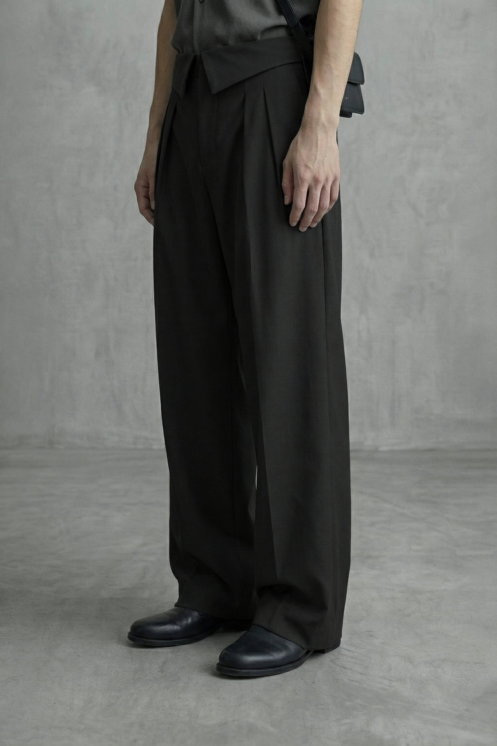 Person wearing black wide-leg pants and black shoes against a gray background