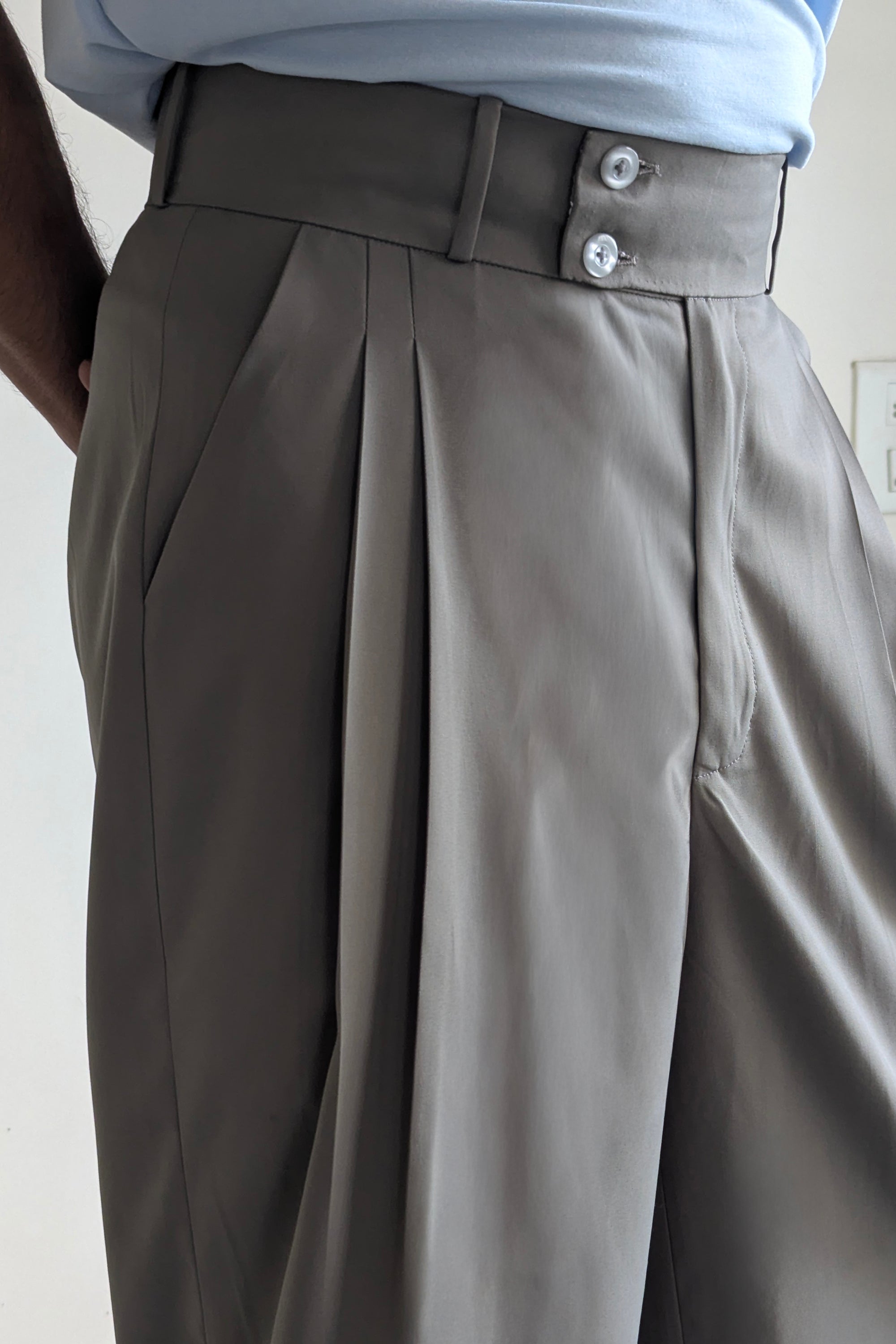 Close-up of gray pleated pants with a belt and light blue shirt.