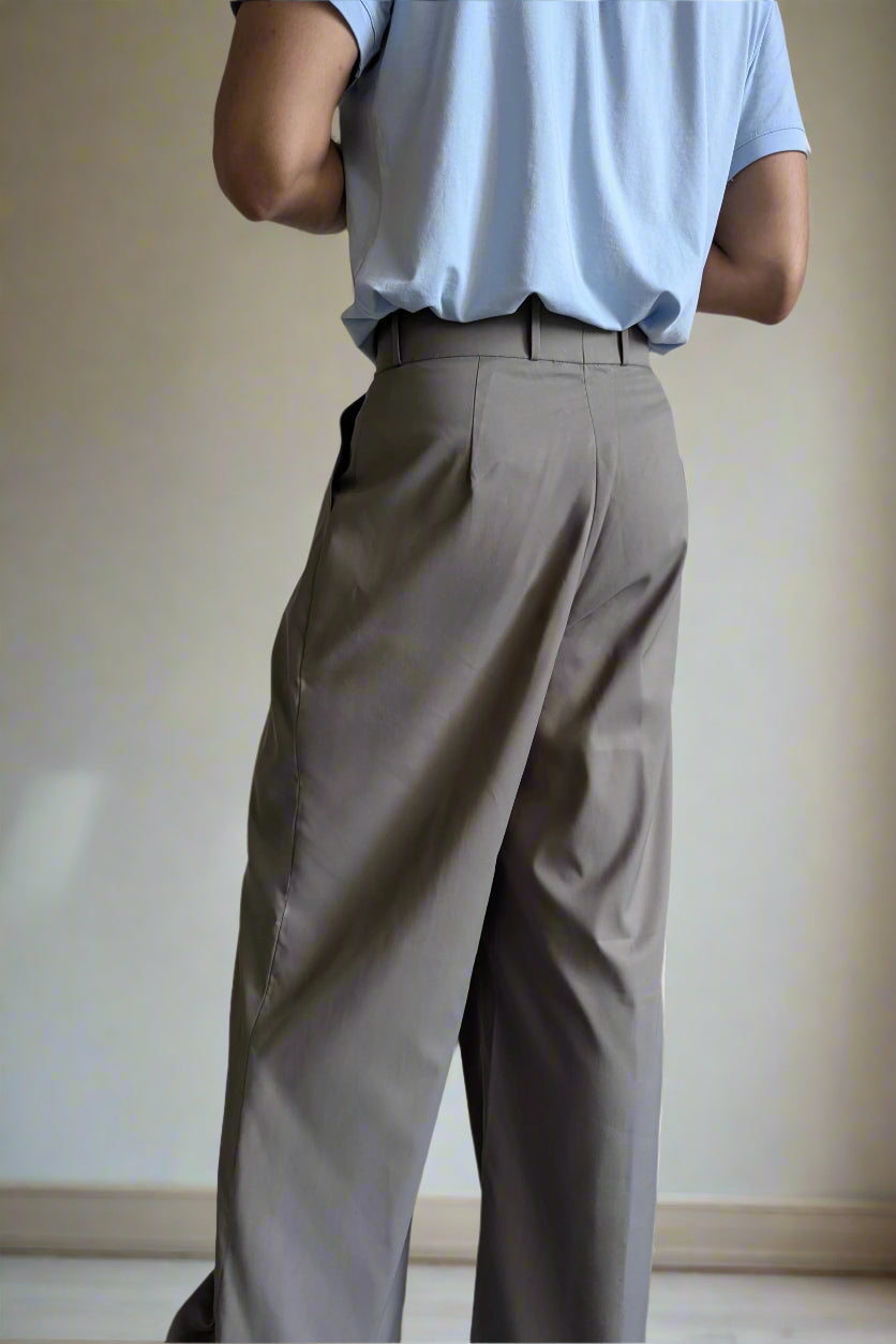 Person wearing light blue shirt and beige pants against a plain wall.