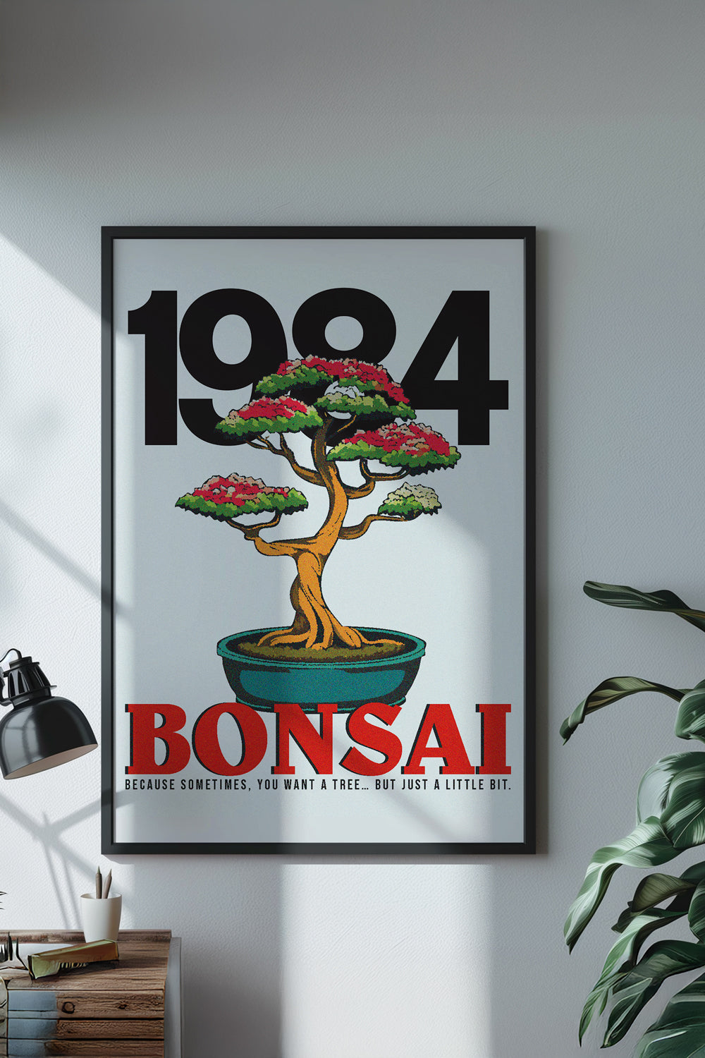 Framed '1984 Bonsai' poster on a wall with a plant and lamp in the background.
