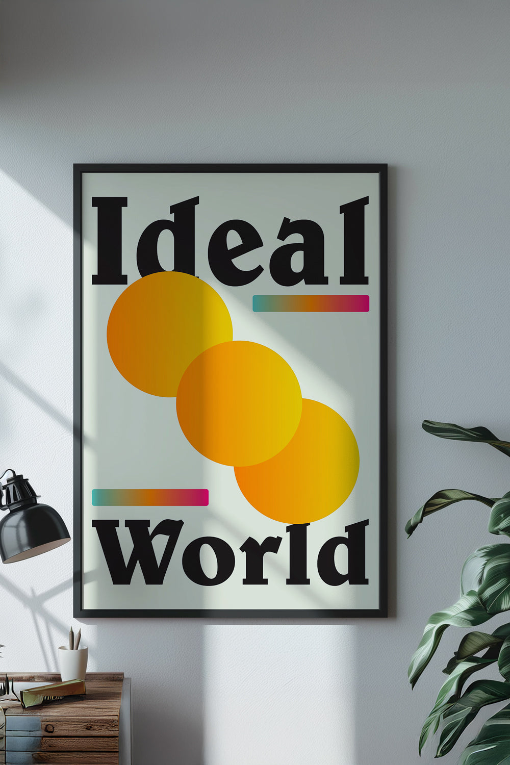 Framed poster with 'Ideal World' design on a wall with a plant and lamp in the background