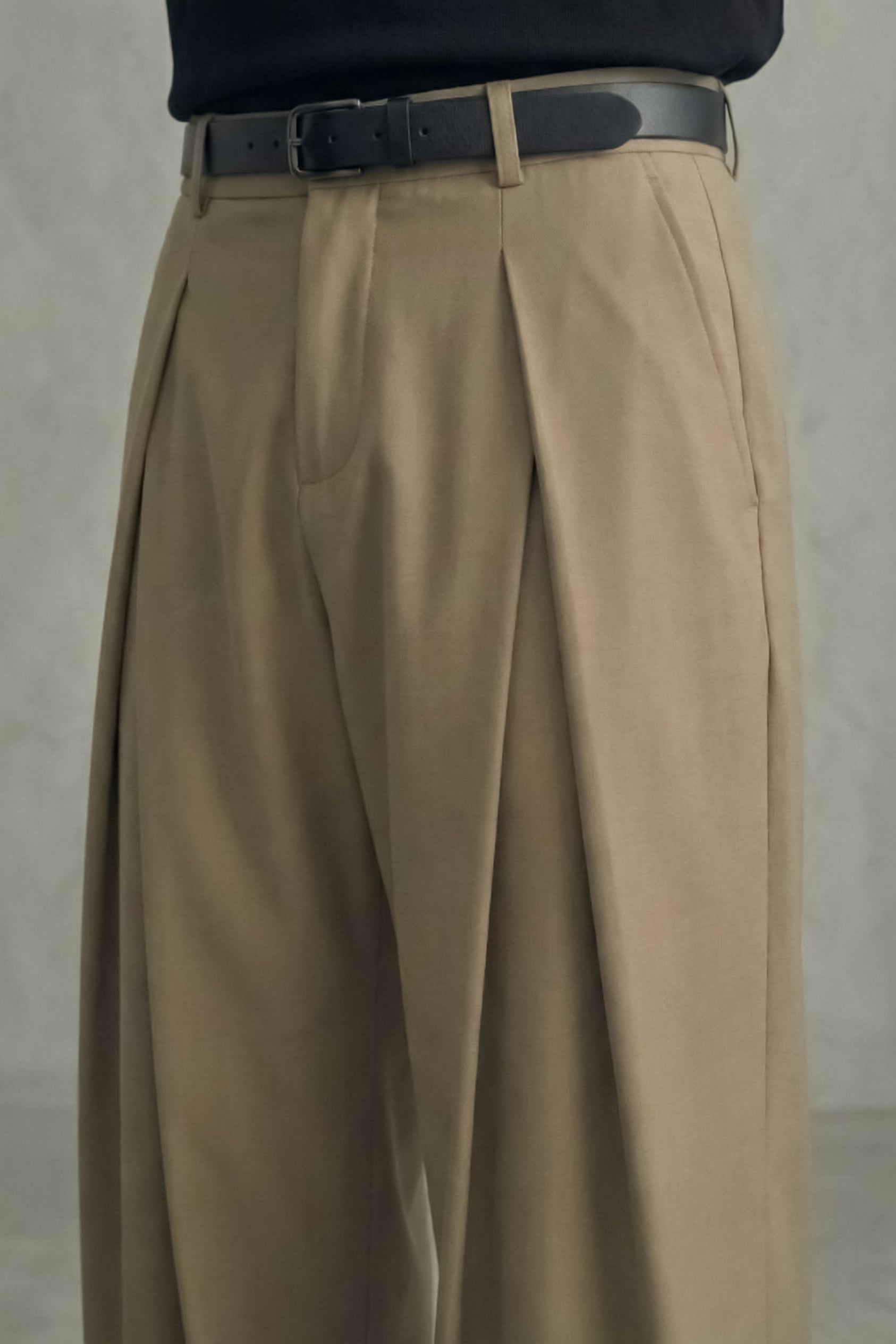 Beige pleated pants with a black belt on a neutral background