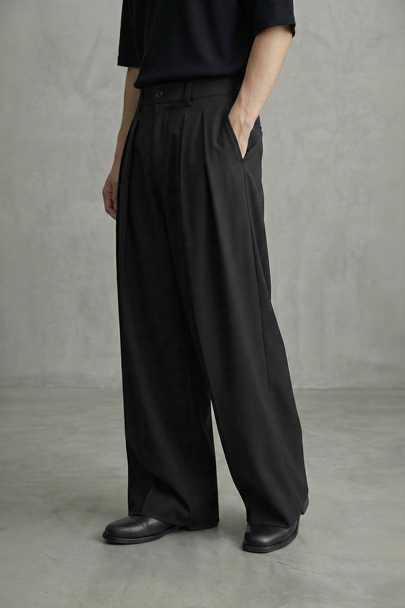 Person wearing black wide-leg pants and black shoes against a gray background