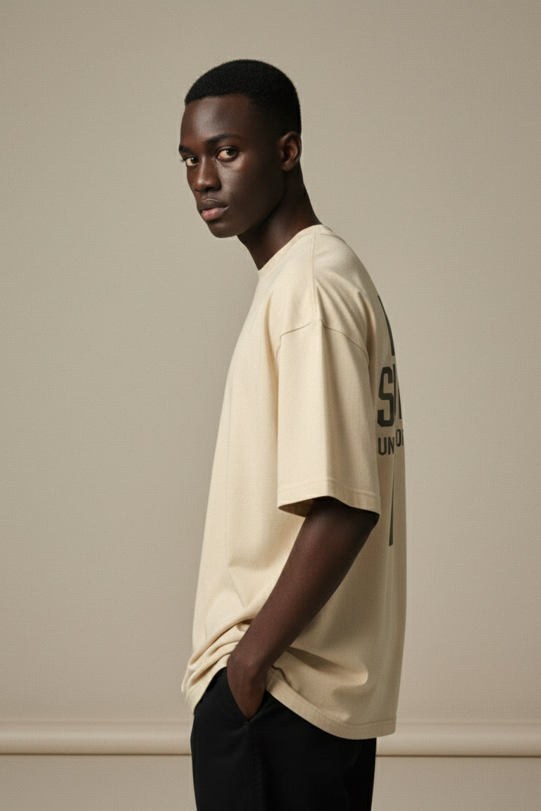 Man wearing a beige t-shirt with a logo on a plain background