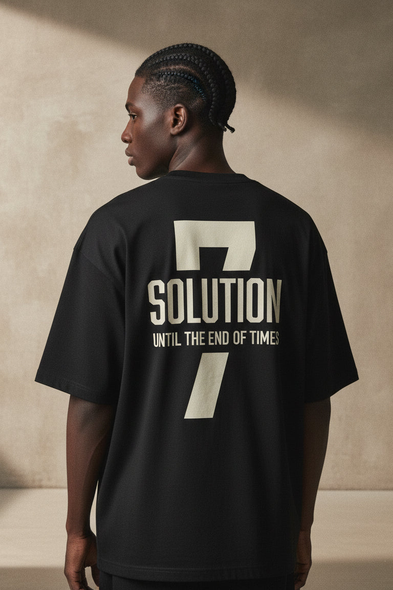 Person wearing a black t-shirt with '7 Solution' text on the back against a beige wall.