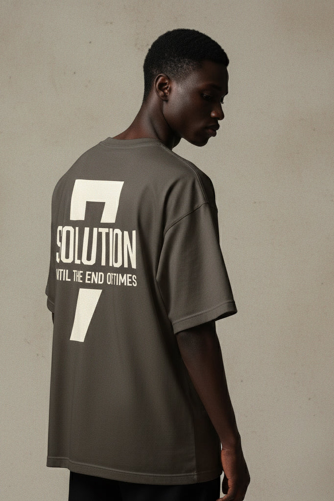 Man wearing a brown t-shirt with a white graphic and text on the back against a beige background