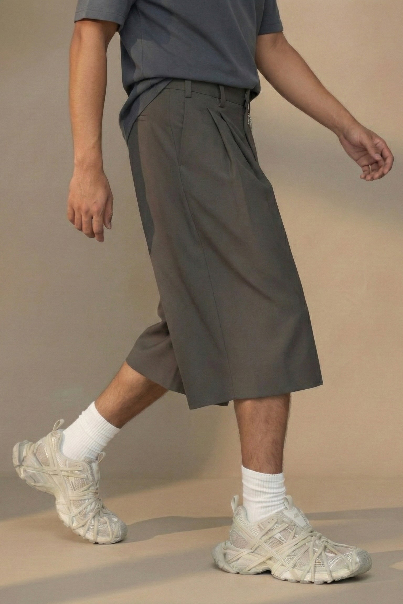 Person wearing brown shorts and beige shoes on a neutral background