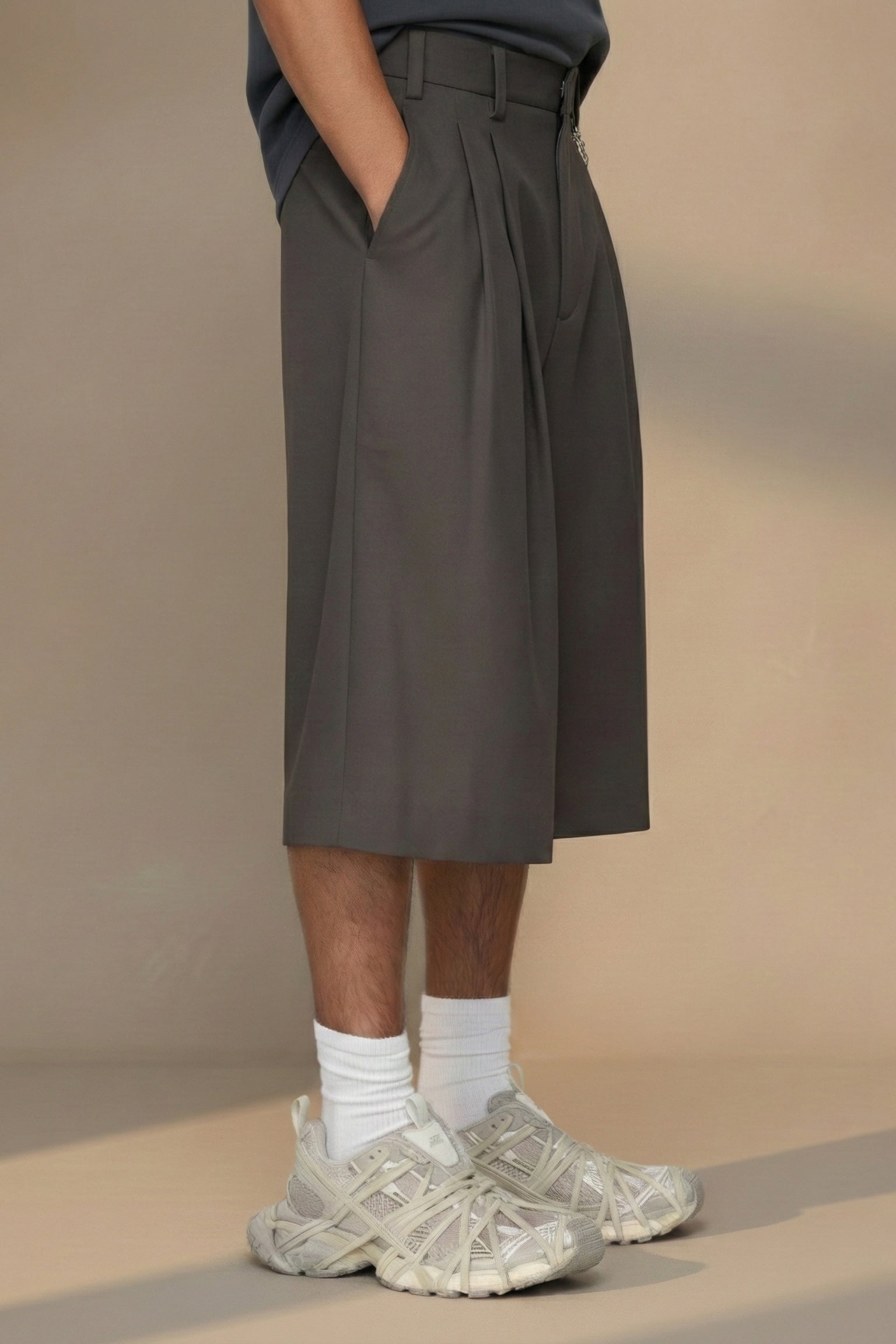 Person wearing a dark gray pleated skirt with white sneakers on a beige background