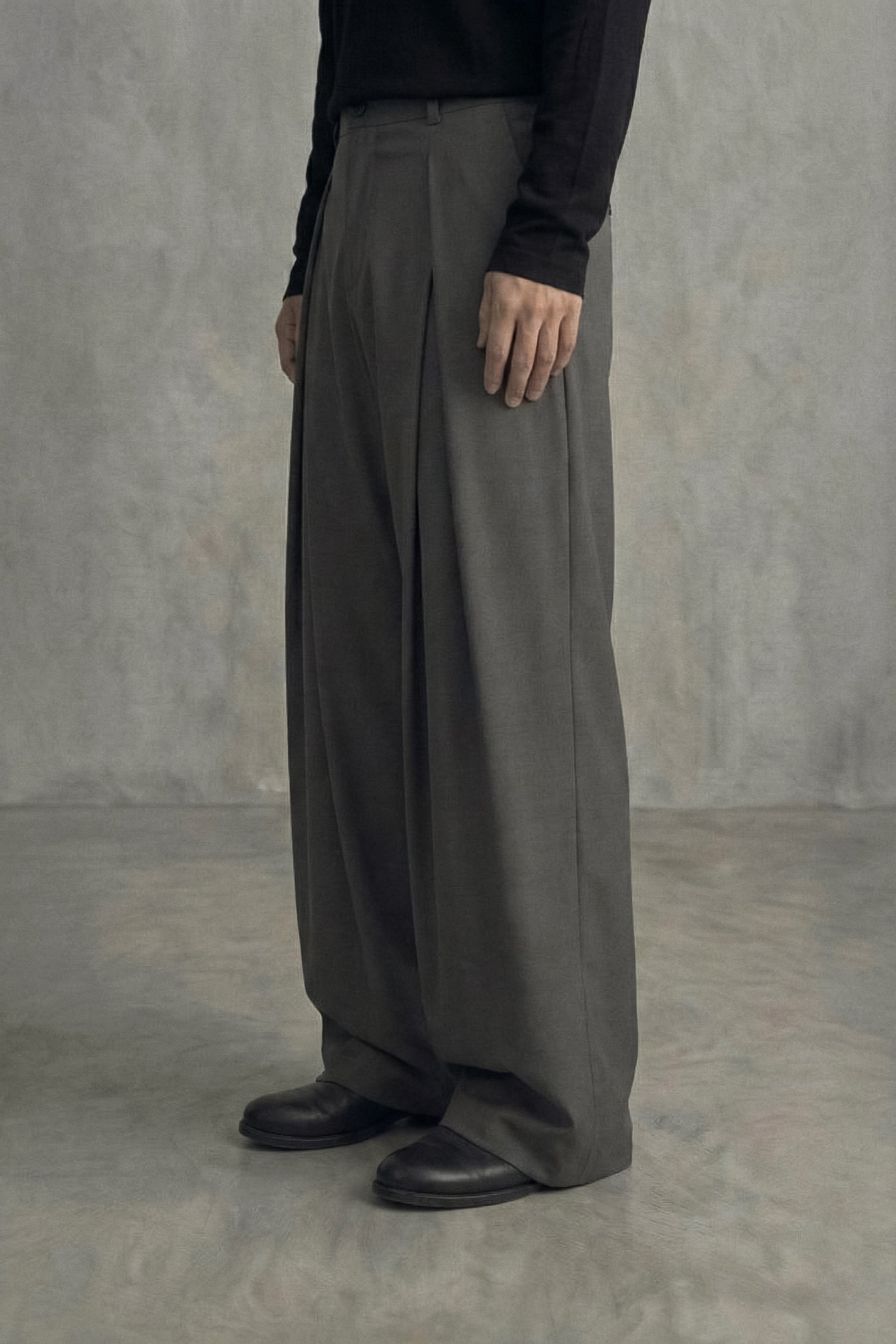 Person wearing gray wide-leg pants and black shoes against a plain background