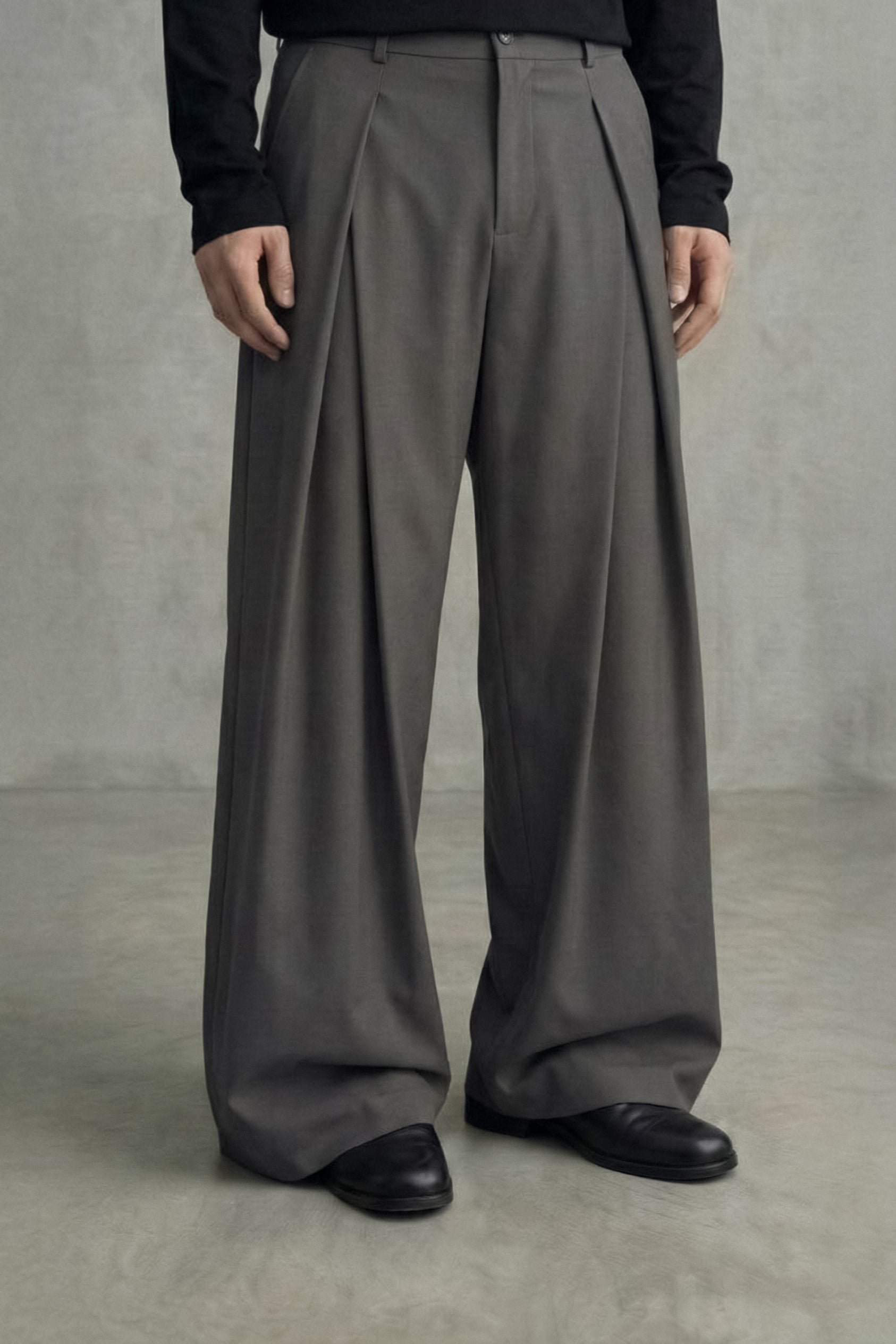 Person wearing gray wide-leg pants and black shoes against a plain background