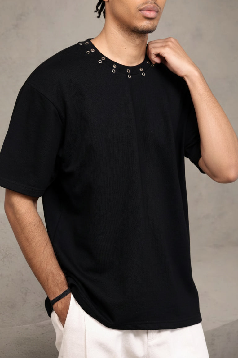 Person wearing a black t-shirt with grommet details on a gray background