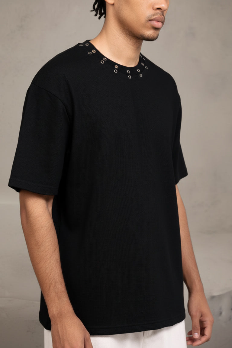 Person wearing a black t-shirt with decorative elements on a plain background