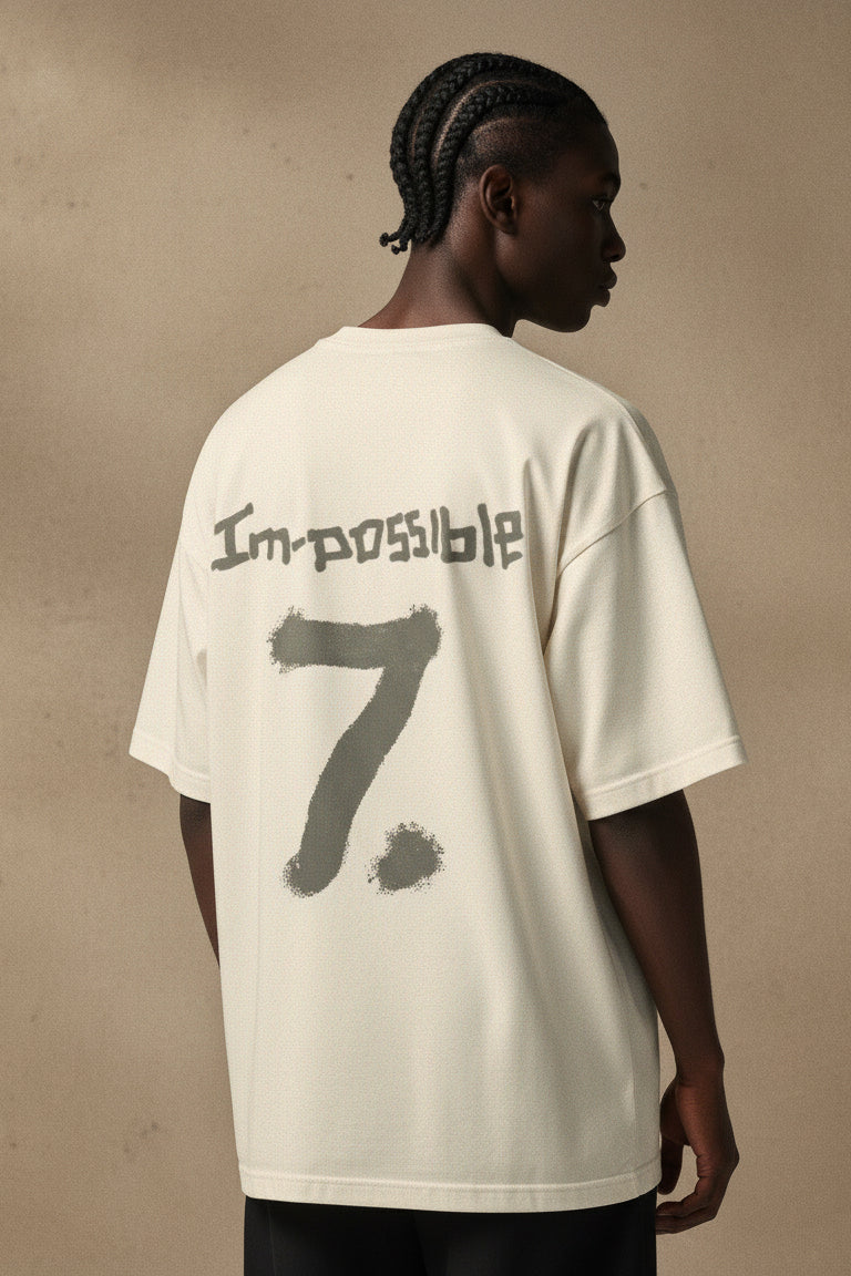 Person wearing a white t-shirt with 'Impossible 7' text on the back against a beige background