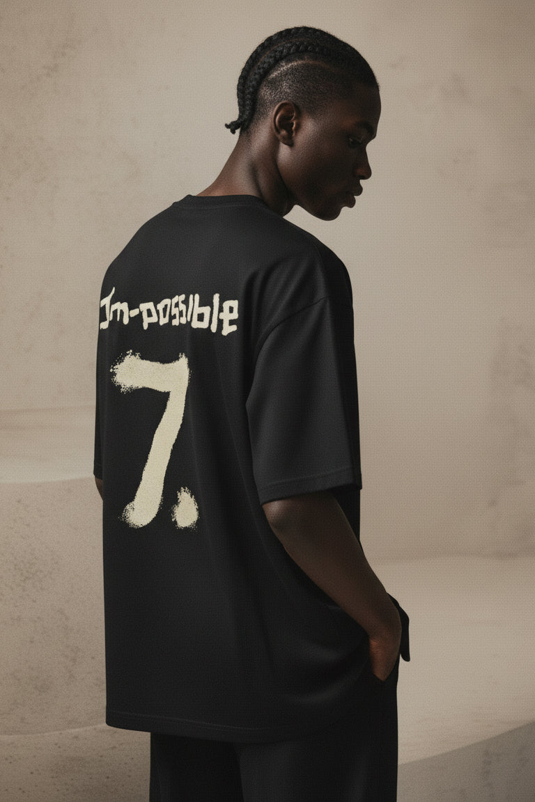 Person wearing a black t-shirt with 'I'm-possible 7' text on the back against a beige background