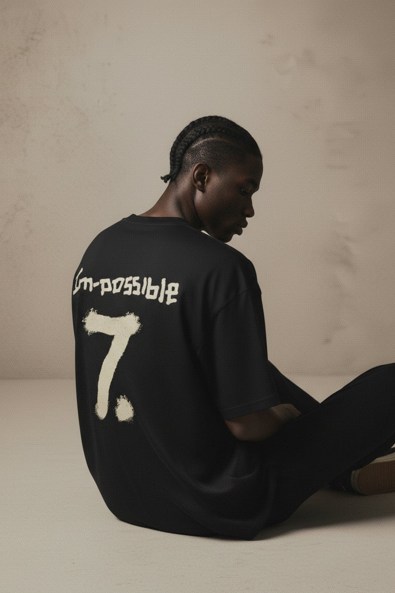 Person wearing a black shirt with 'im-possible 7' text sitting on a beige background