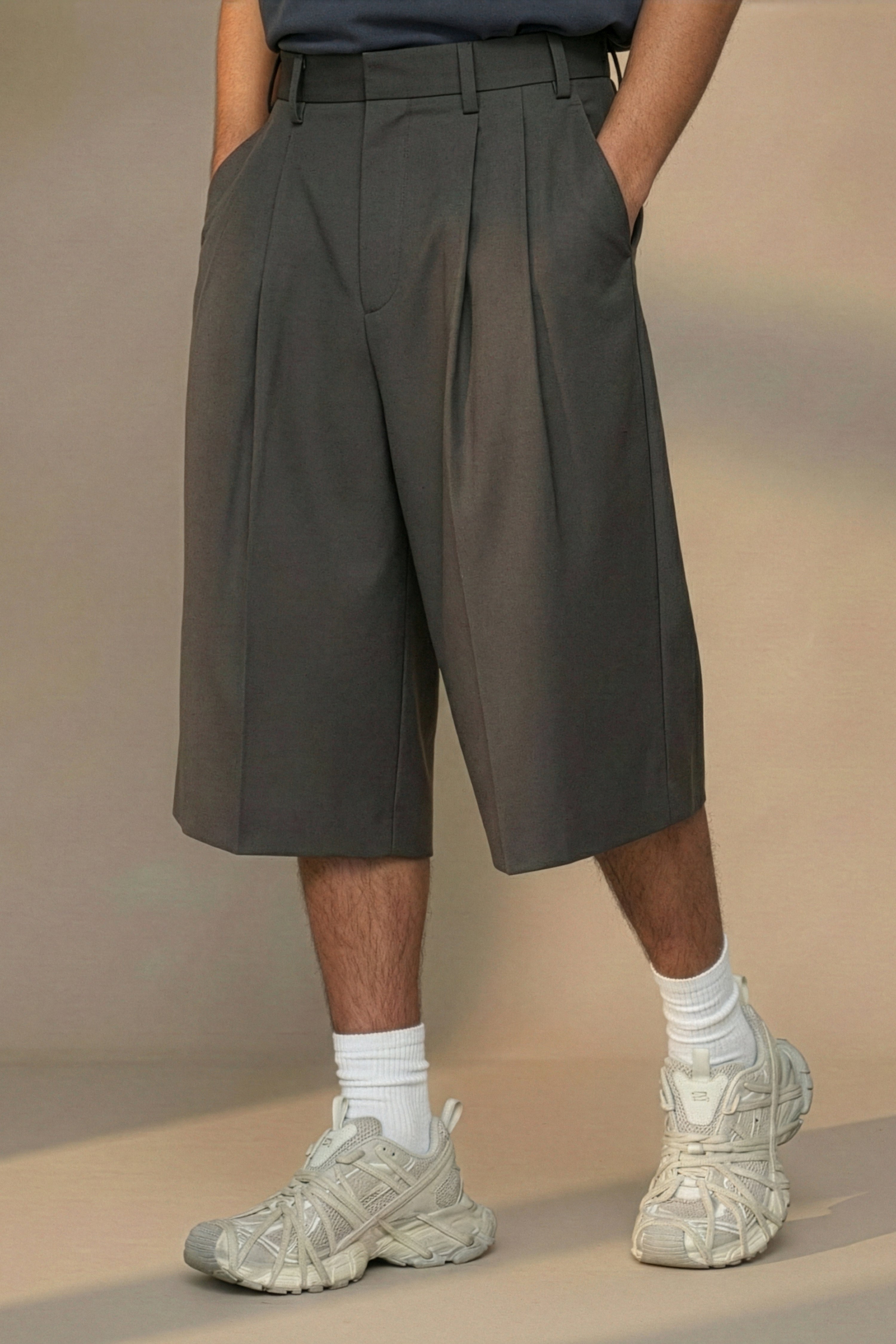 Person wearing dark pleated shorts with a neutral background