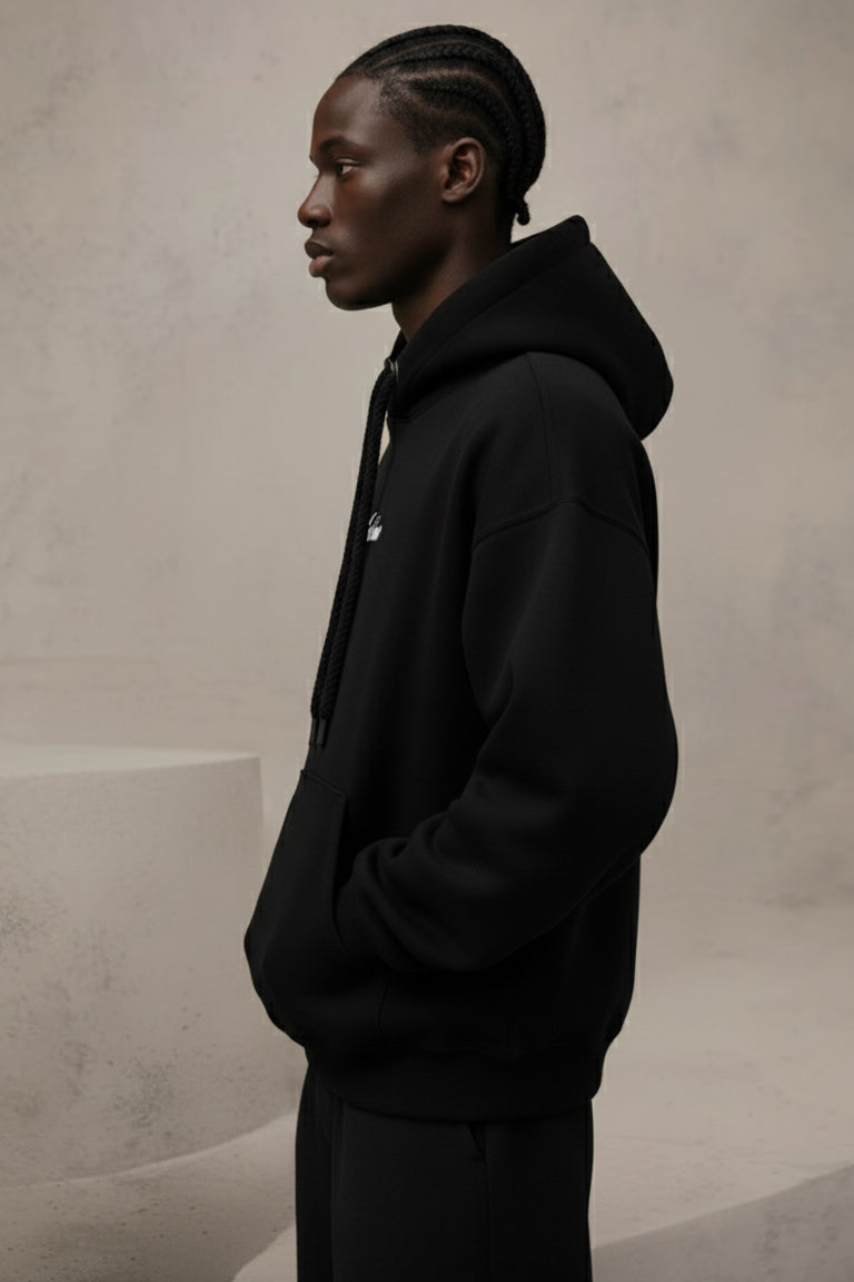 Person wearing a black hoodie with a logo on a neutral background