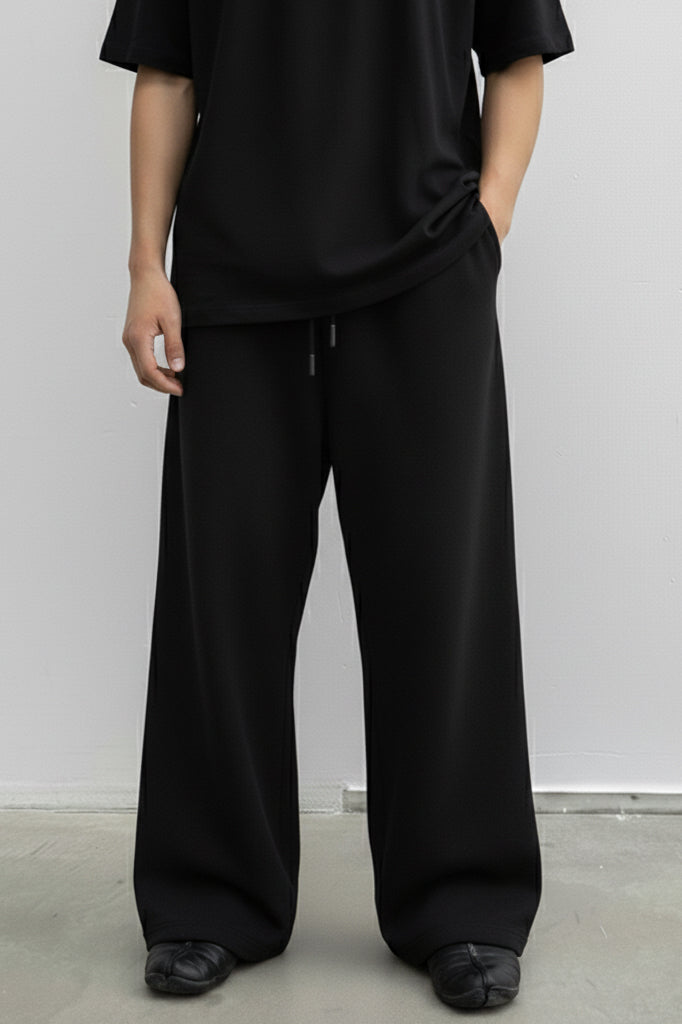Person wearing a black outfit with wide-leg pants against a white background