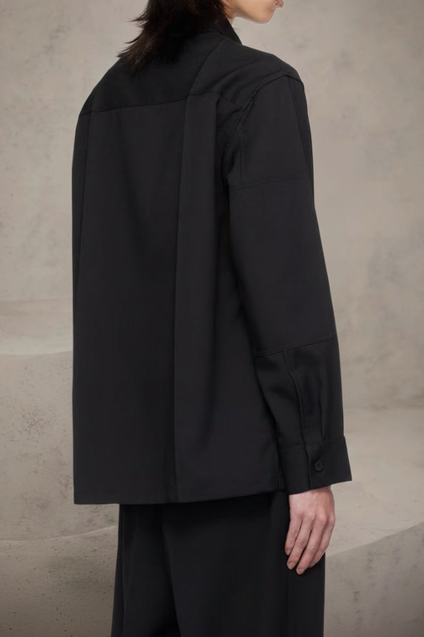 Person wearing a black coat against a neutral background