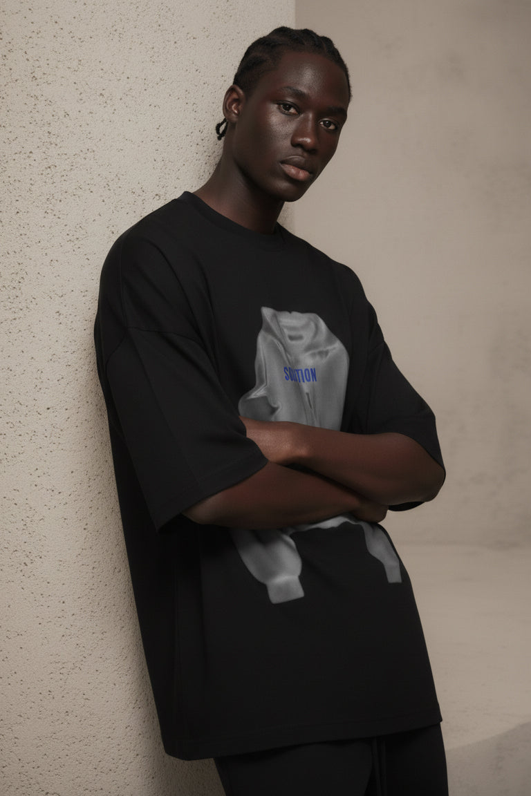 Person wearing a black oversized t-shirt with a graphic design against a beige wall.