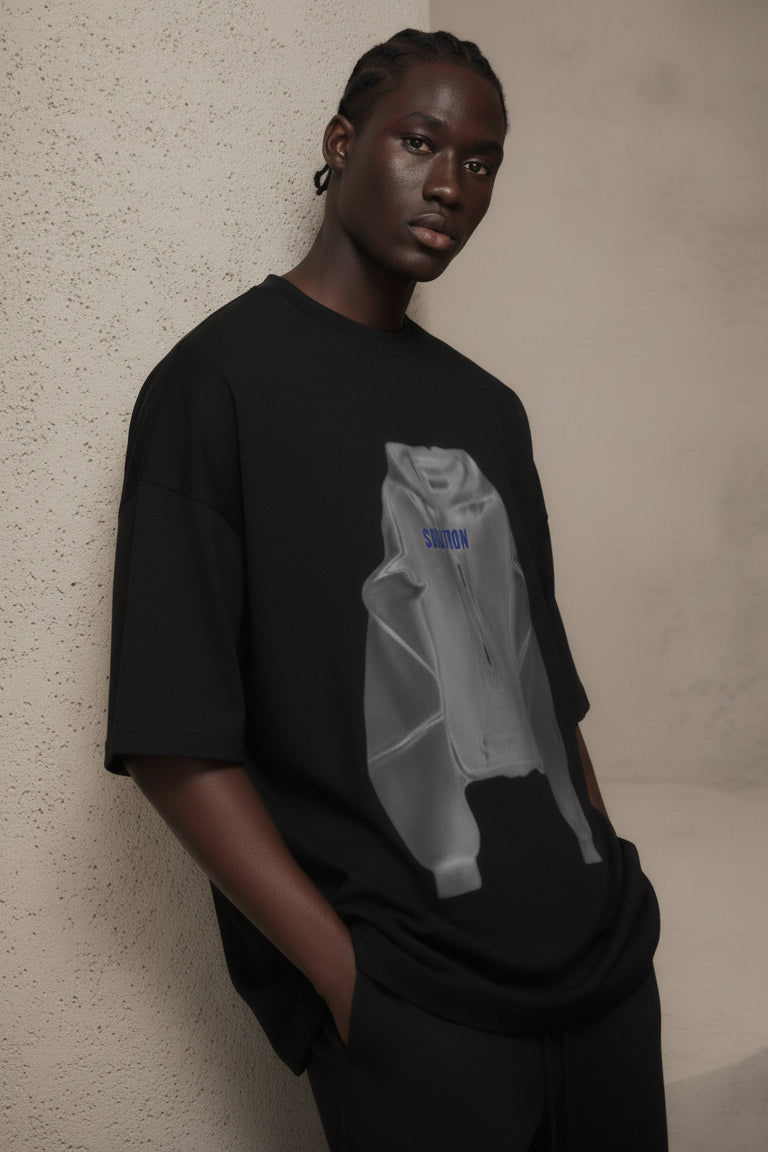 Person wearing a black t-shirt with a graphic design against a beige wall